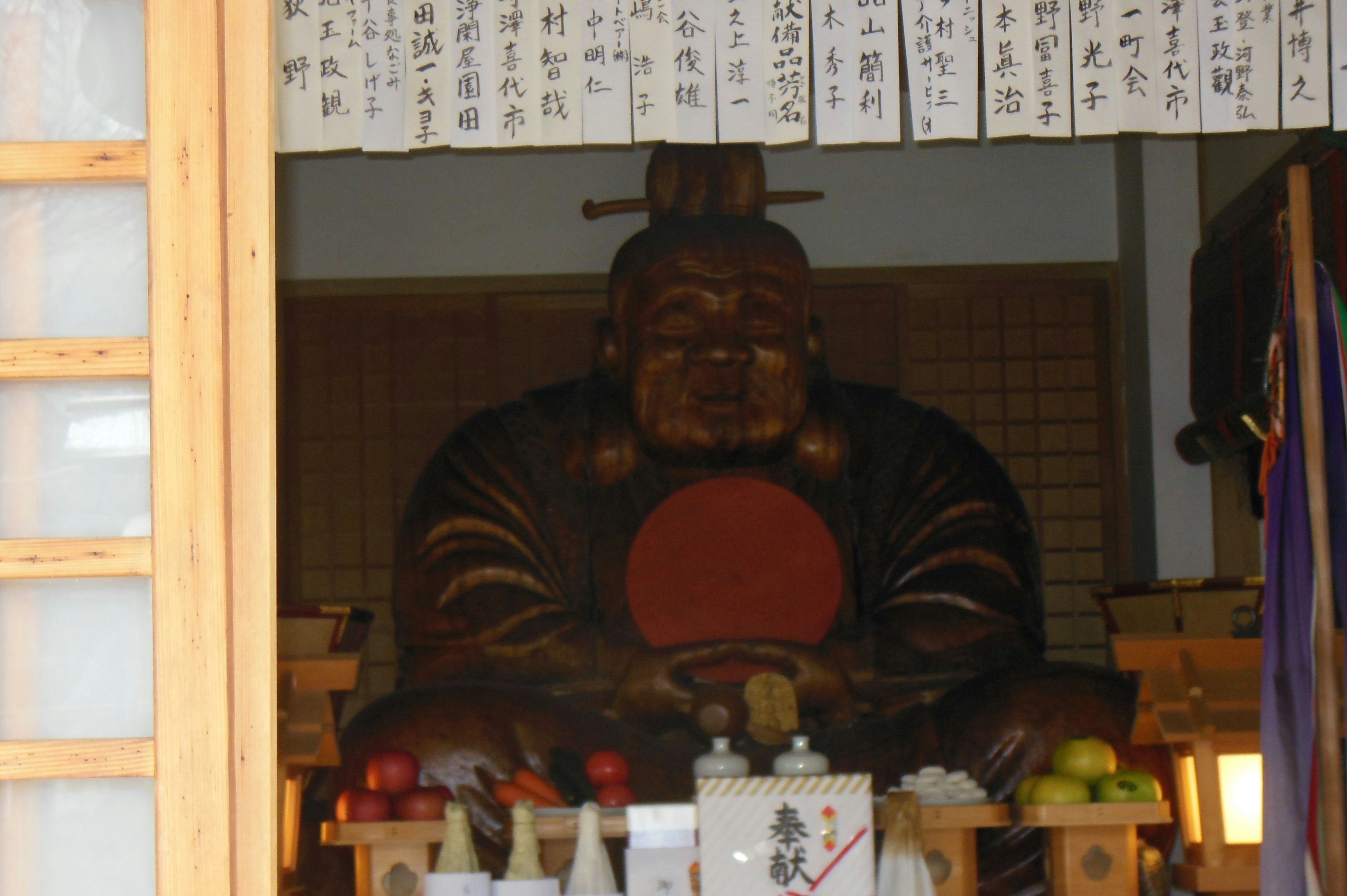 Vista interior de un santuario con una estatua de Buda de madera y una decoración circular roja