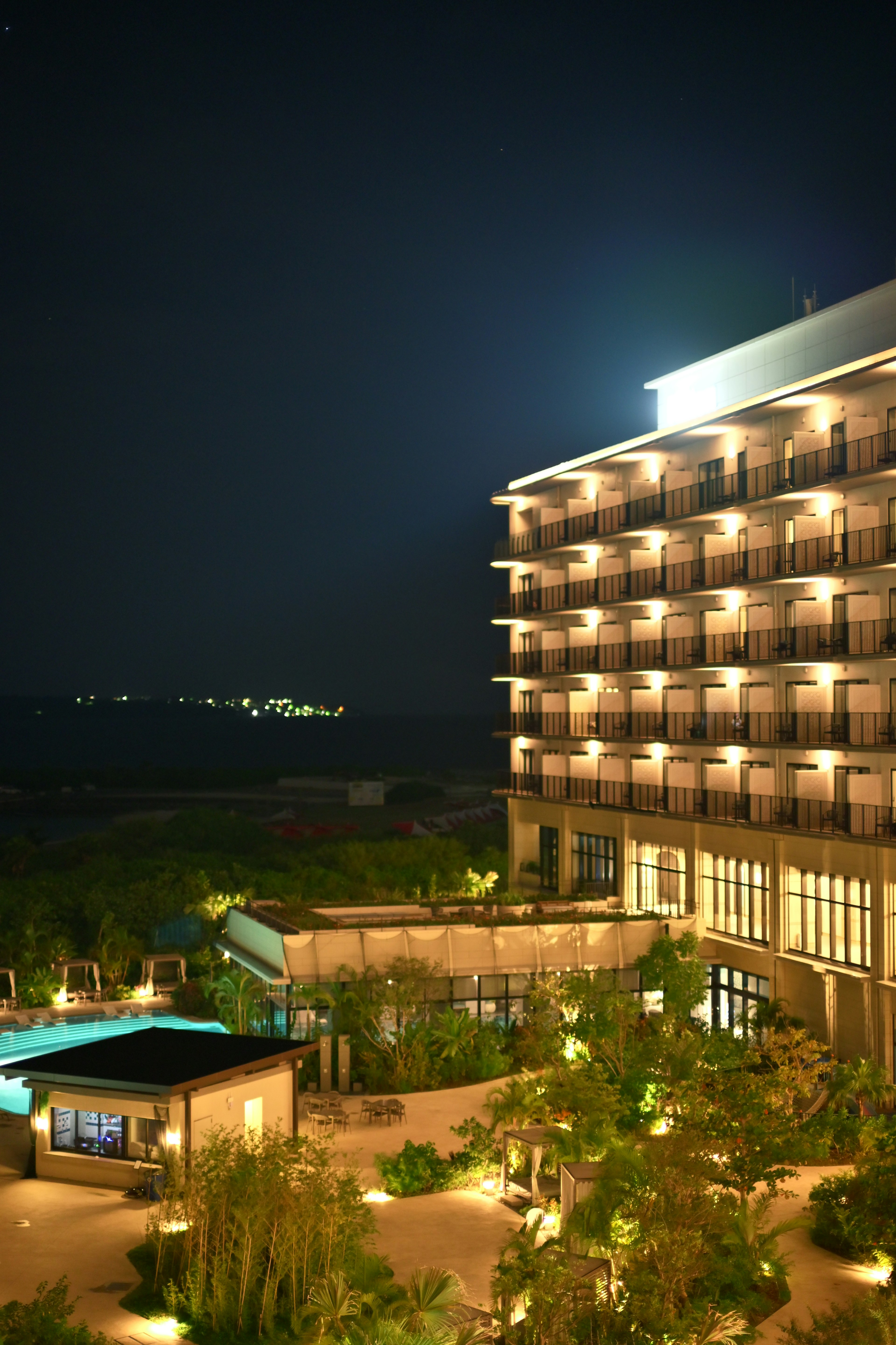 Vista nocturna del exterior de un hotel con jardín y piscina iluminados