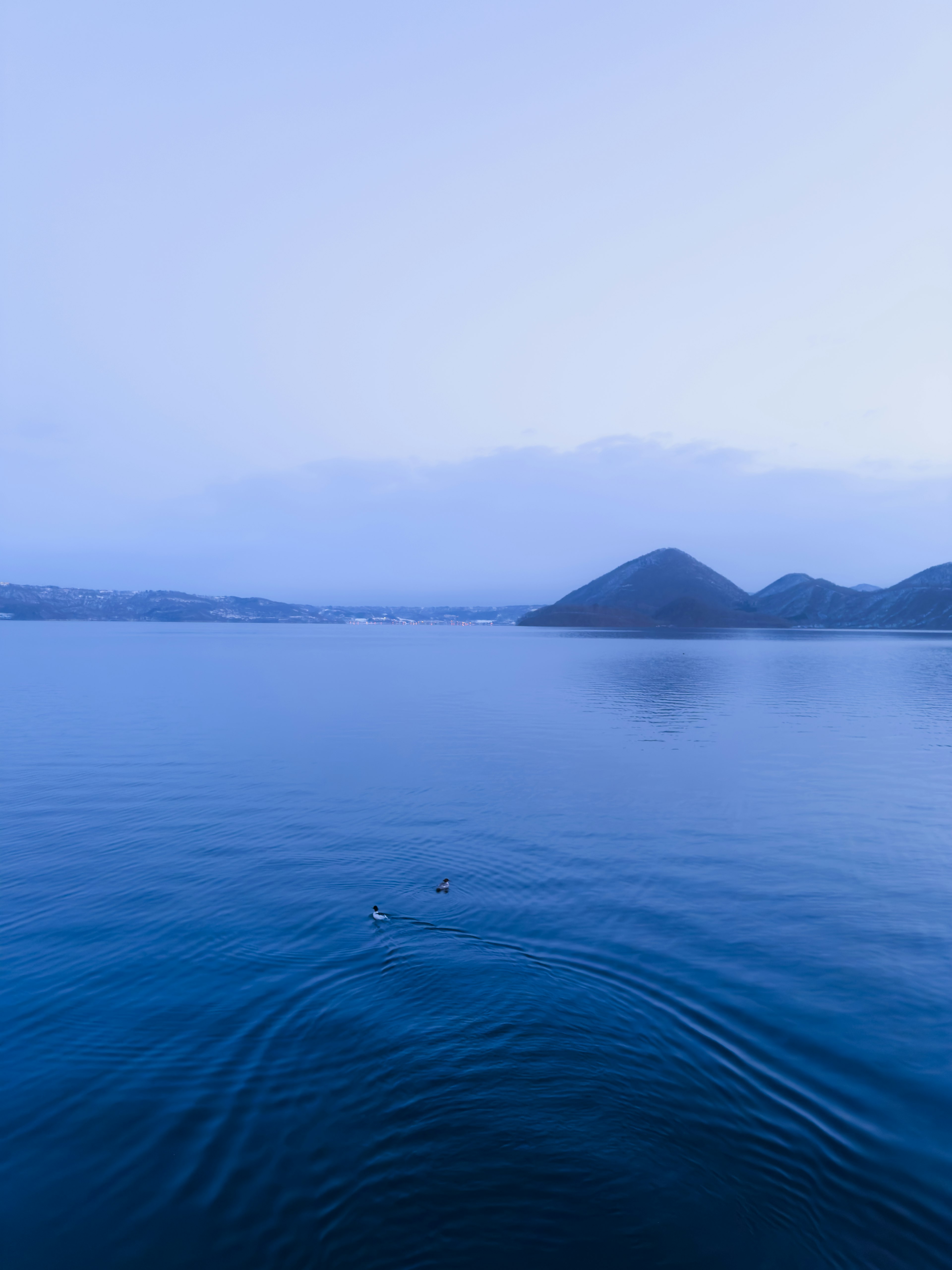 Paisaje de lago azul tranquilo con siluetas de montañas a lo lejos