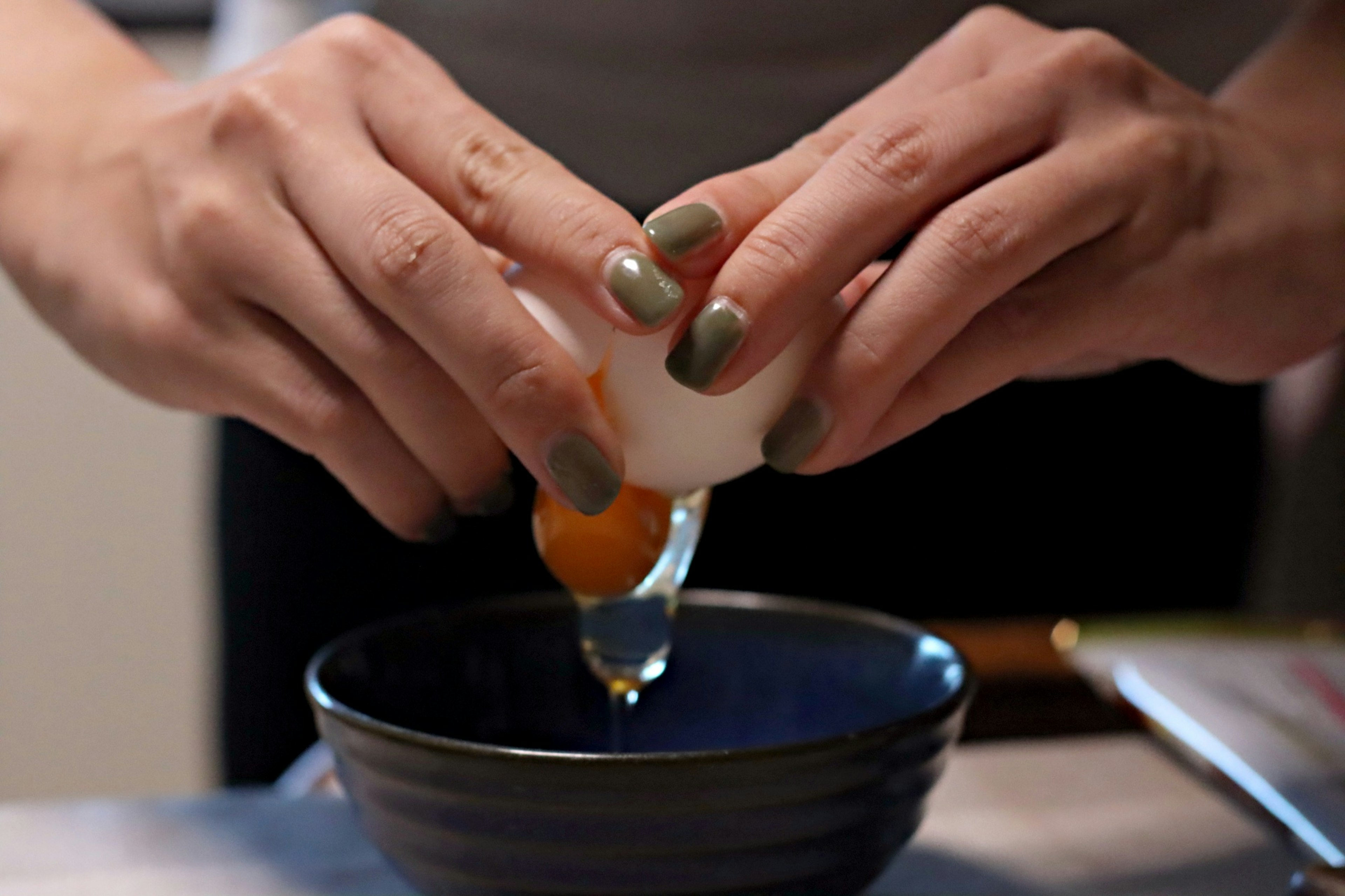 Hands cracking an egg into a blue bowl