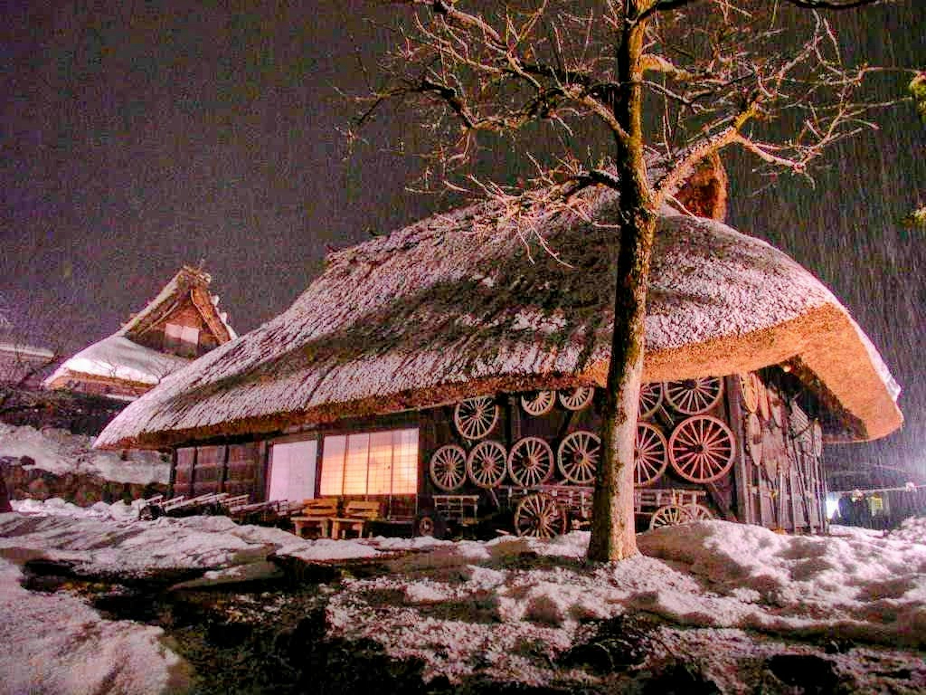 Scène nocturne d'une maison au toit de chaume recouverte de neige avec silhouette d'arbre