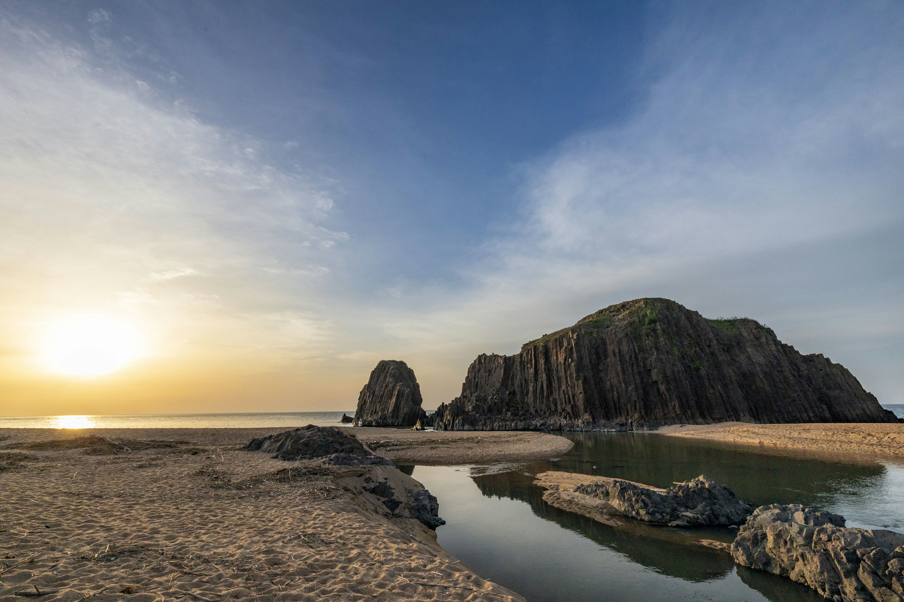 Pemandangan pantai dengan cahaya matahari terbenam dan formasi batuan