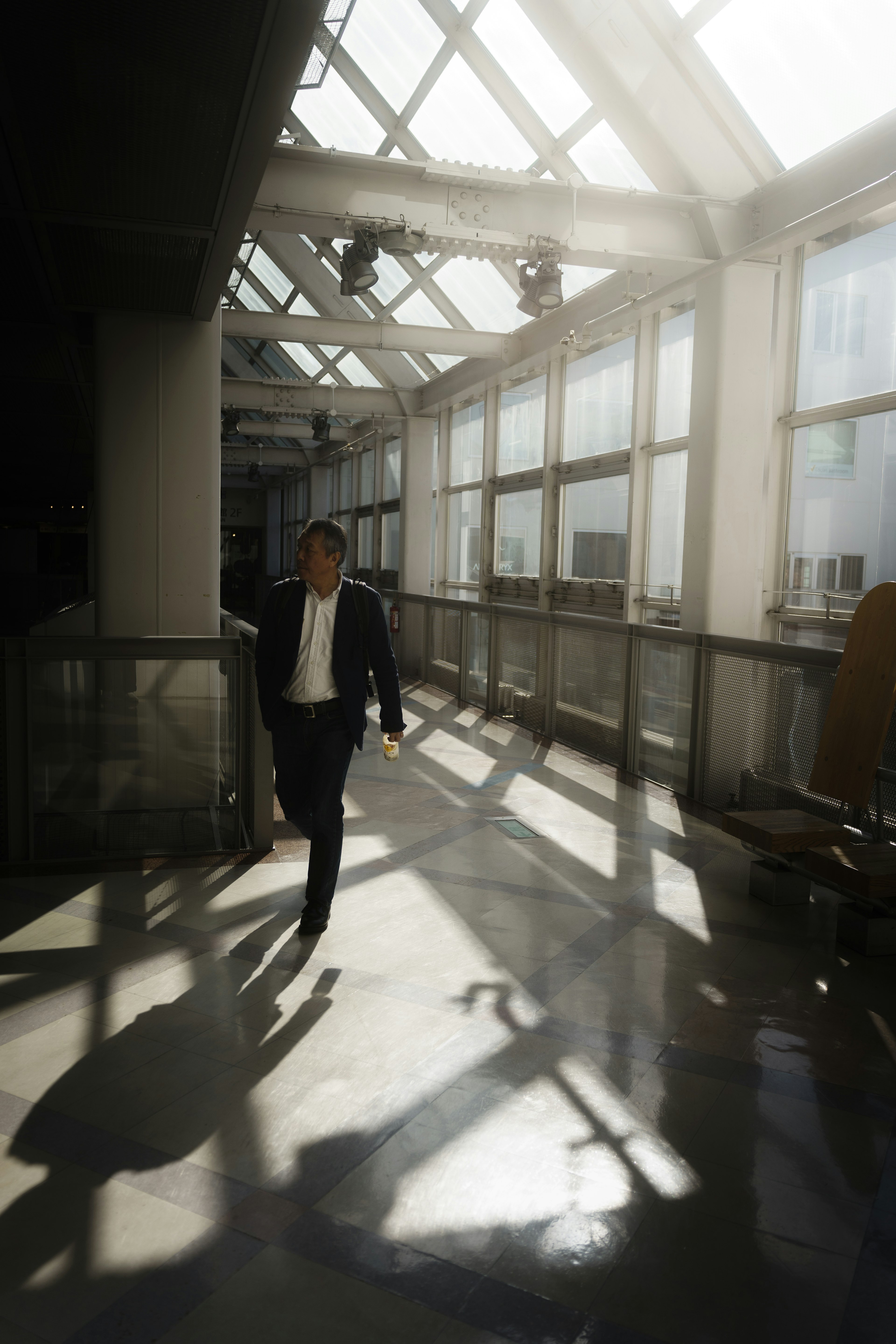 A businessman walking in a glass corridor illuminated by bright light