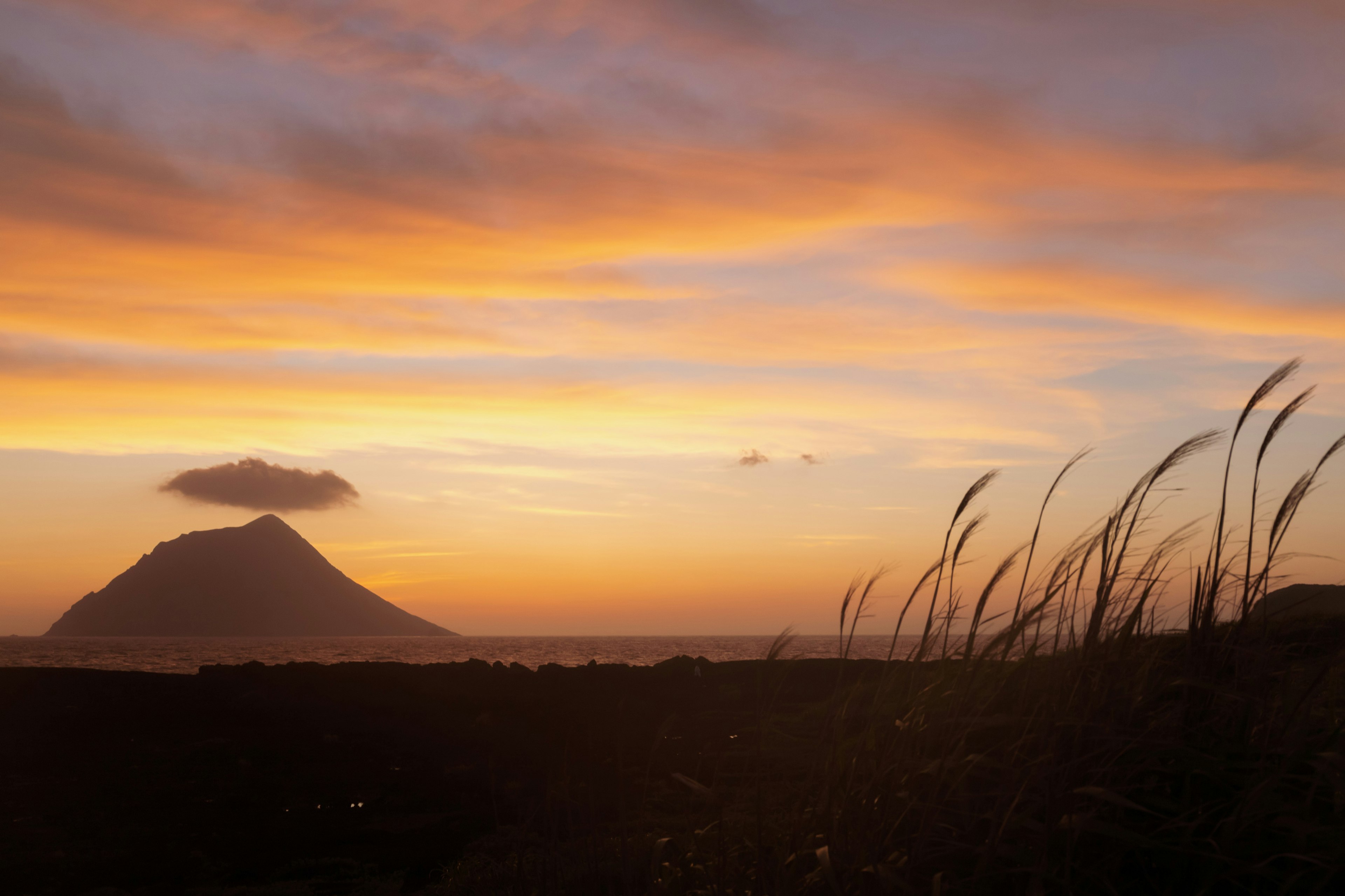 Silueta de un volcán contra un cielo al atardecer y hierba