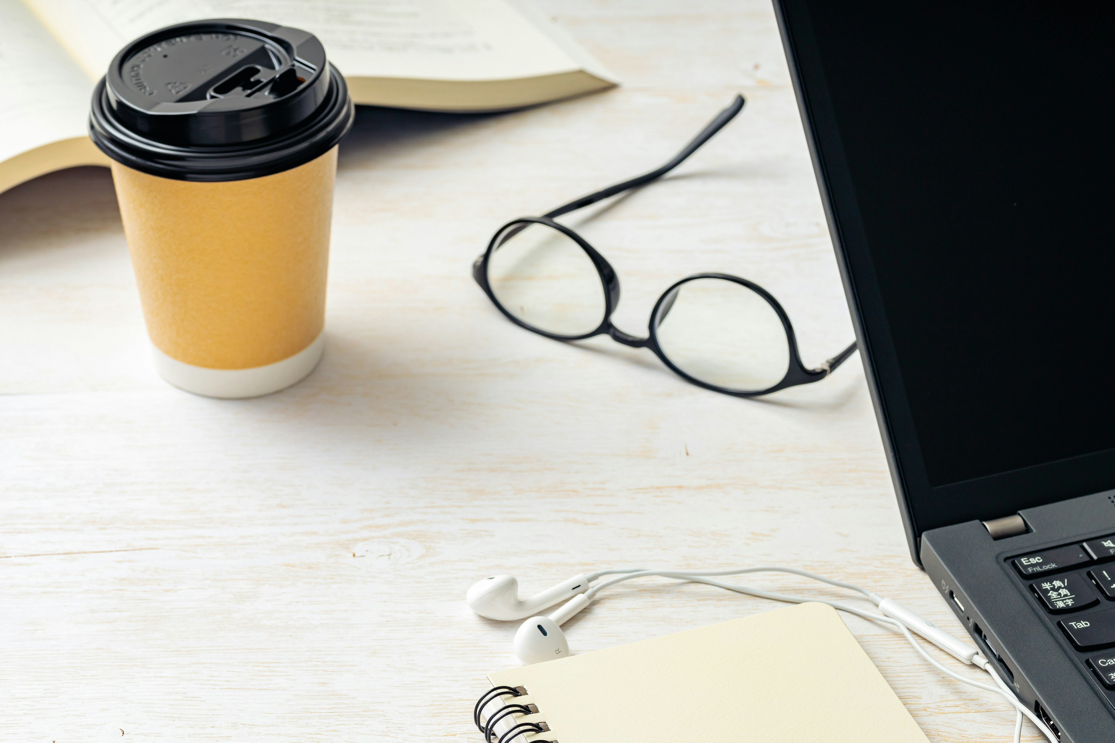 Kaffeetasse und Laptop auf einem Schreibtisch mit Brille und Kopfhörern