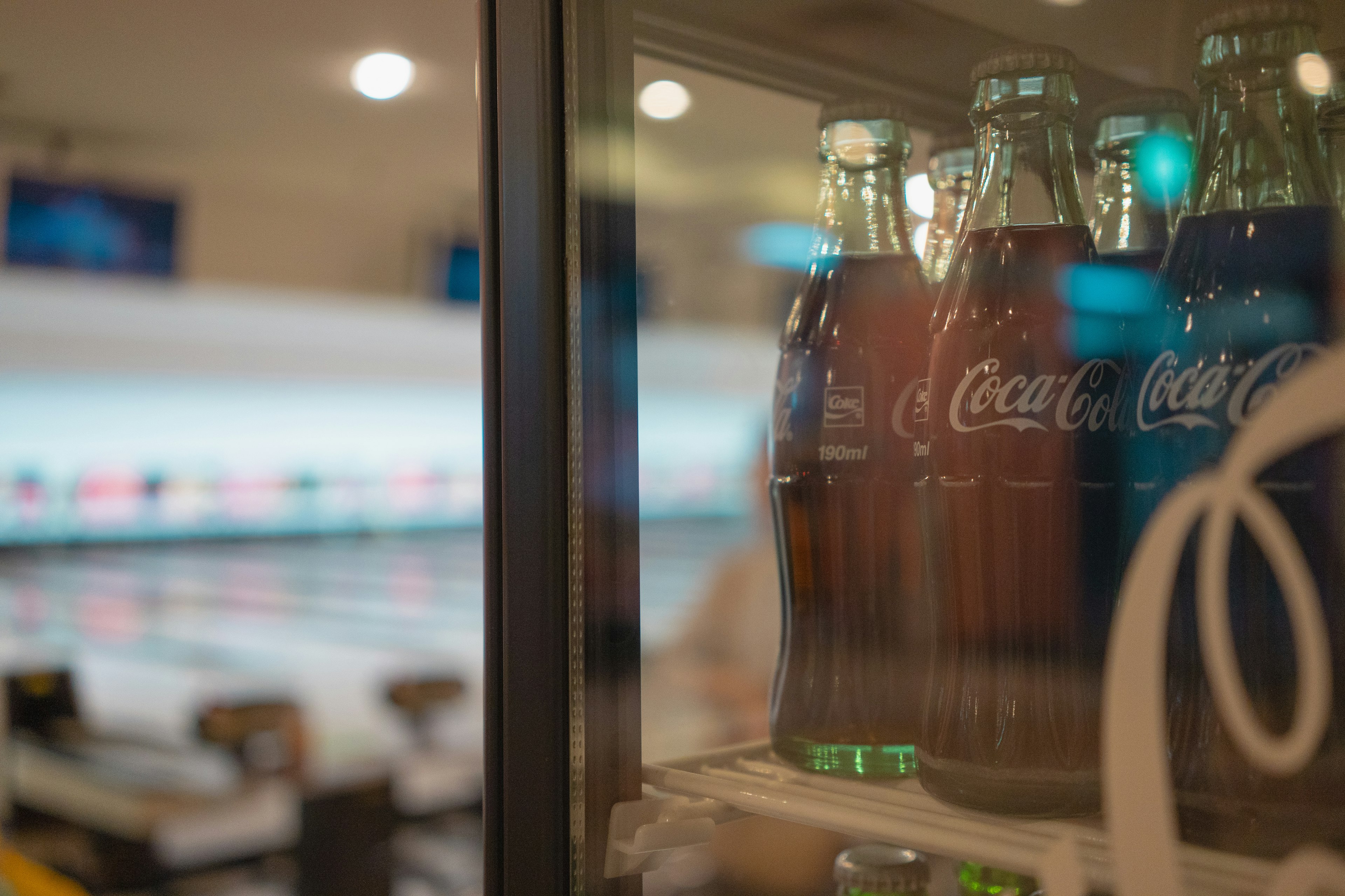 Bottiglie di Coca-Cola in un frigorifero con una pista da bowling sfocata sullo sfondo