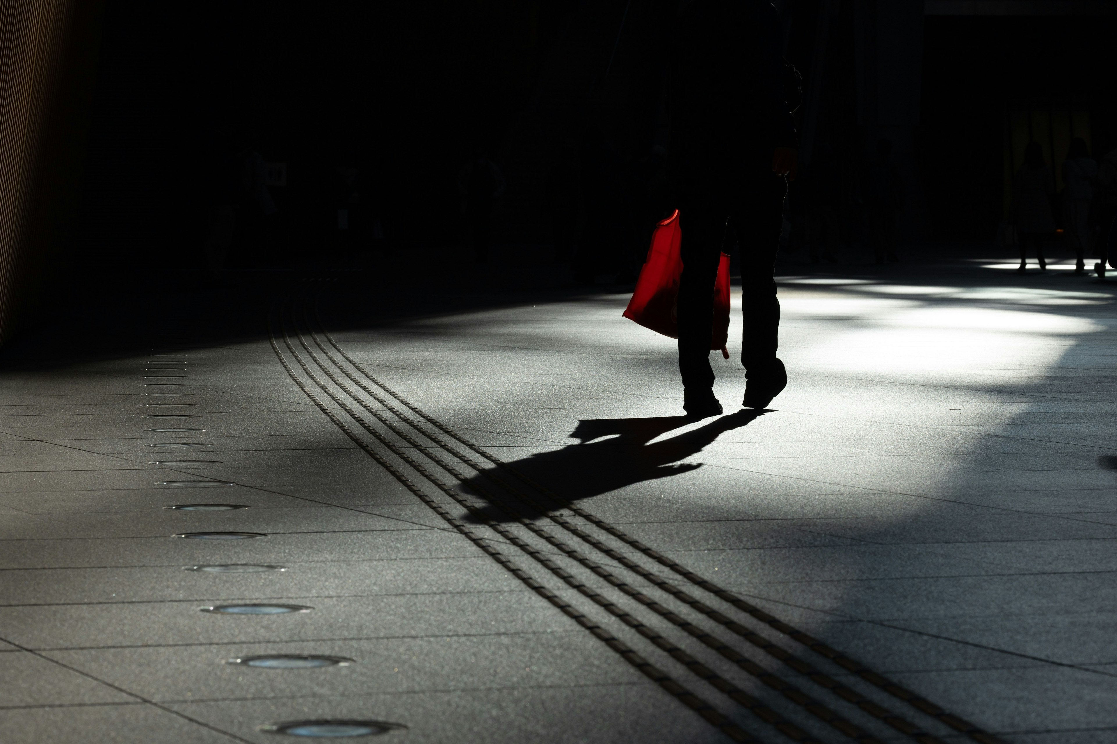 Silueta de una persona caminando con una bolsa roja en sombras
