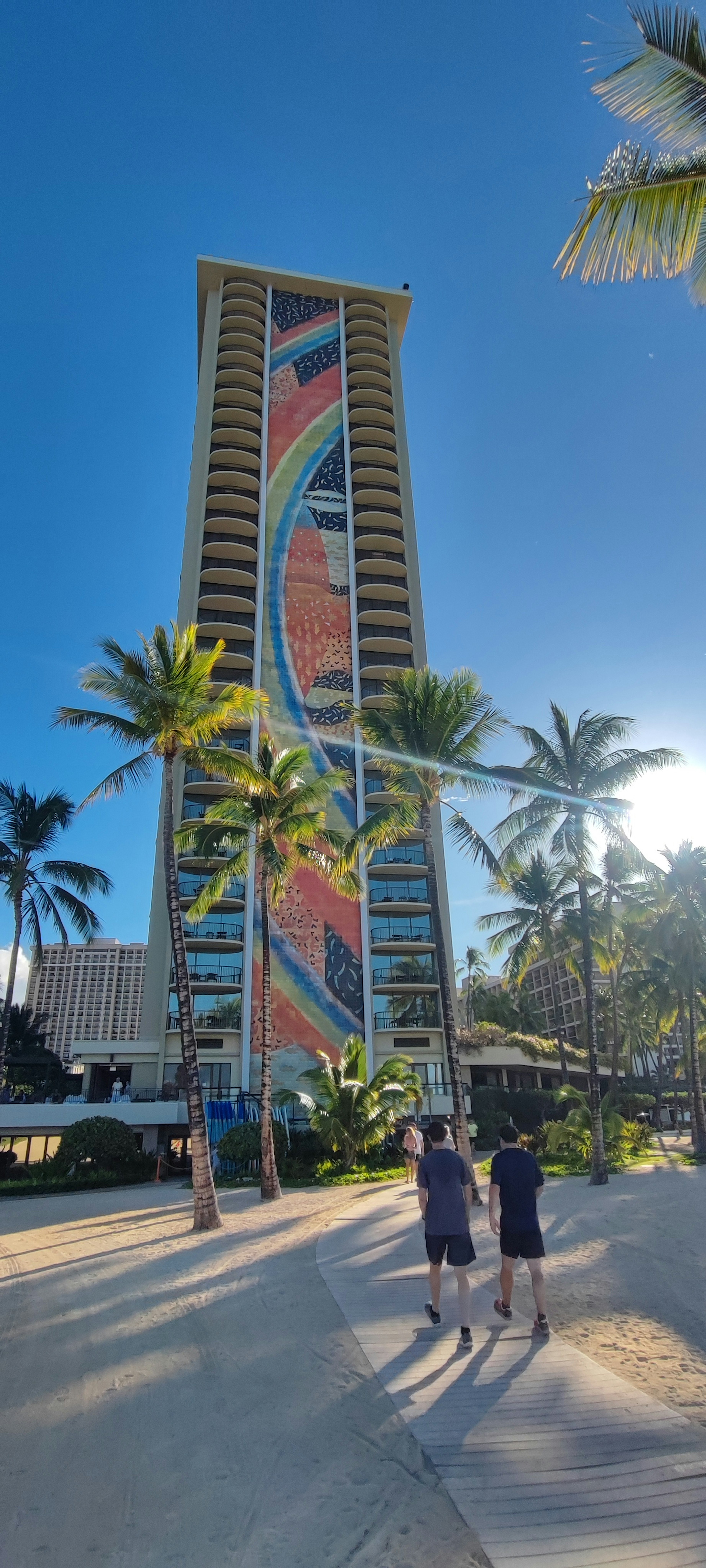 People standing in front of a tall building with palm trees under a blue sky