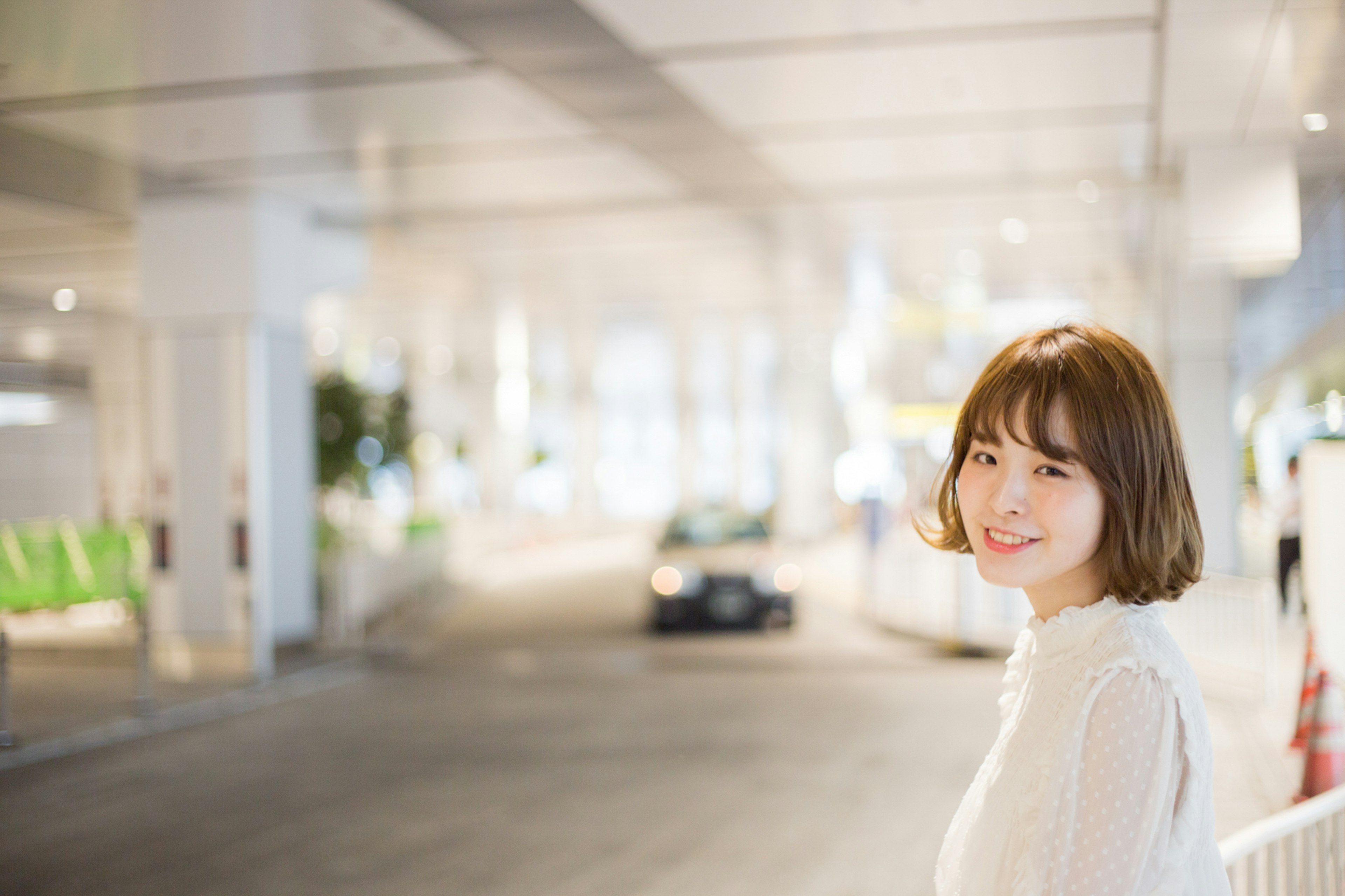 Portrait of a smiling woman in a bright setting with a blurred car and green chairs in the background