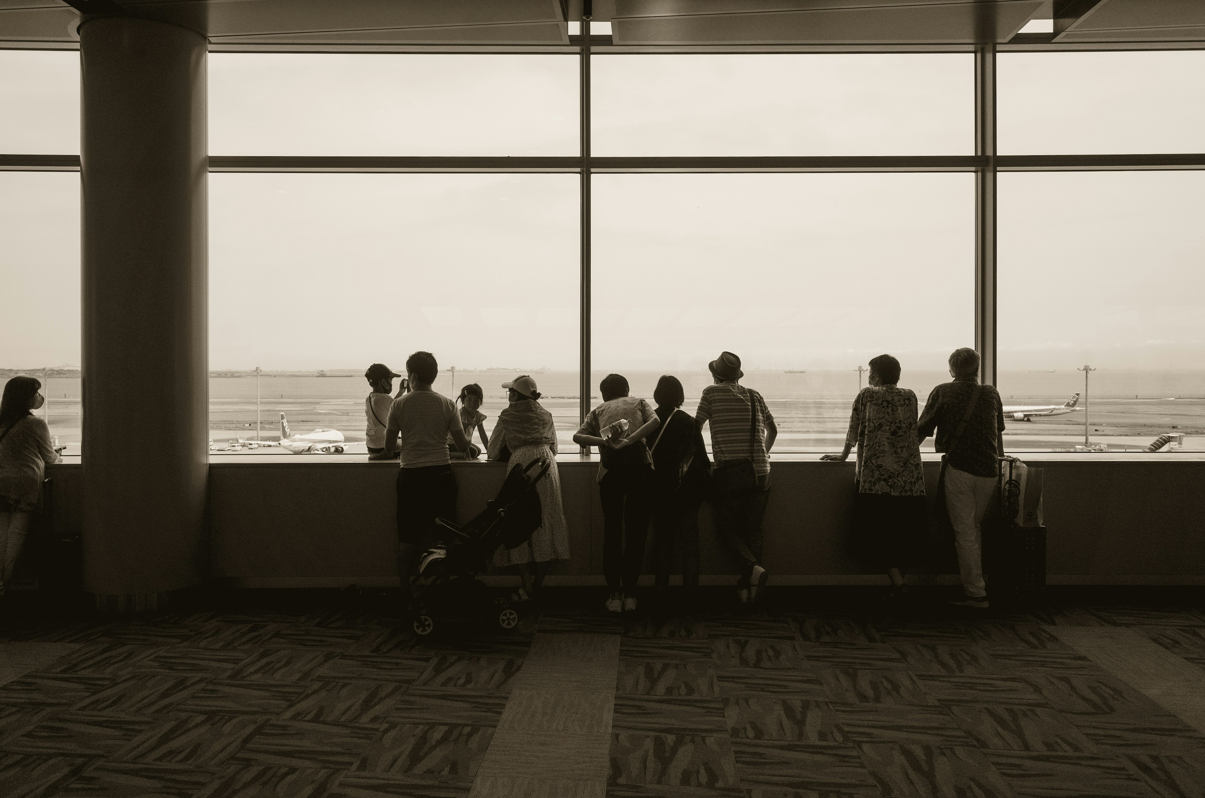 Siluetas de personas de pie junto a una ventana del aeropuerto