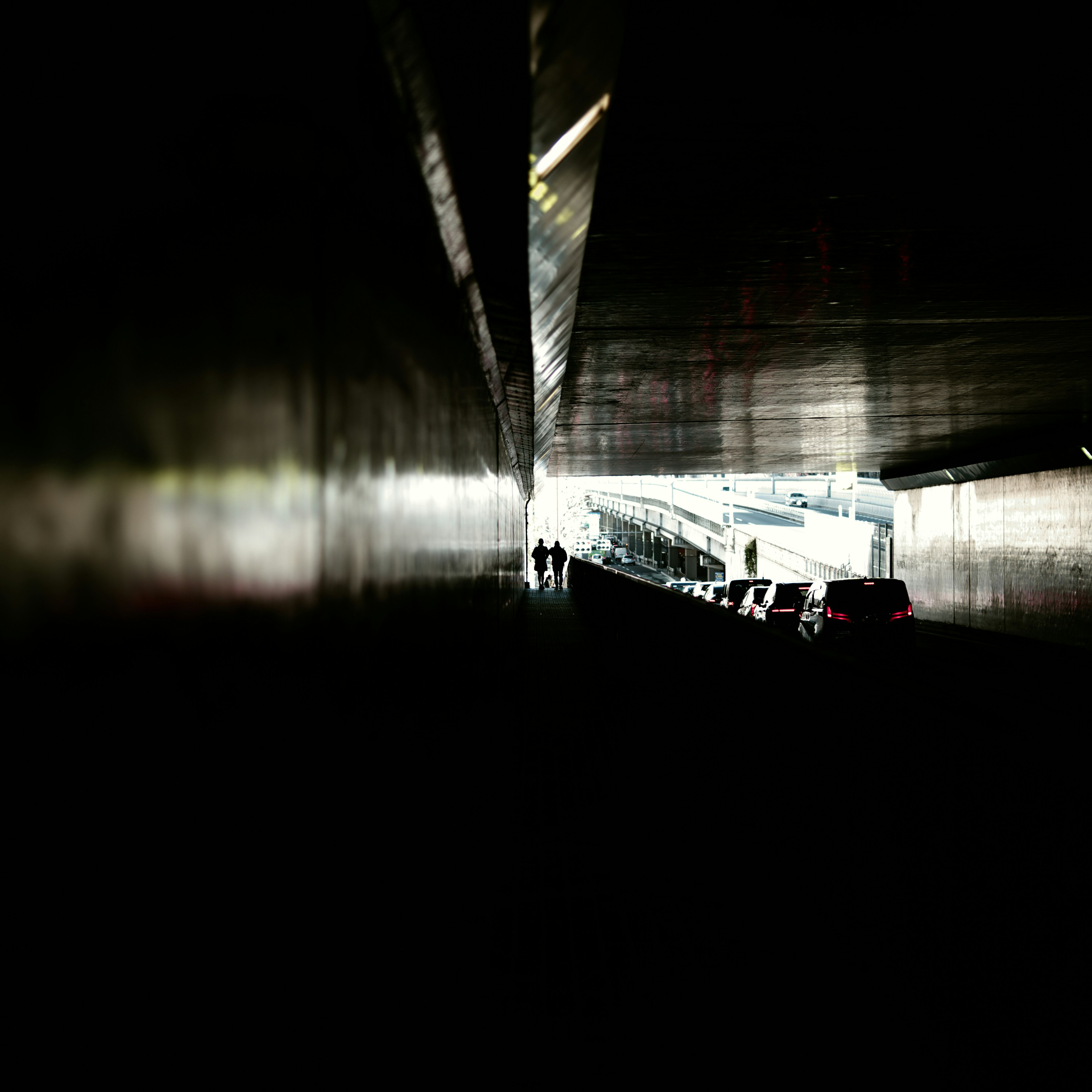 Tunnel sombre avec des personnes et une voiture se dirigeant vers une sortie lumineuse