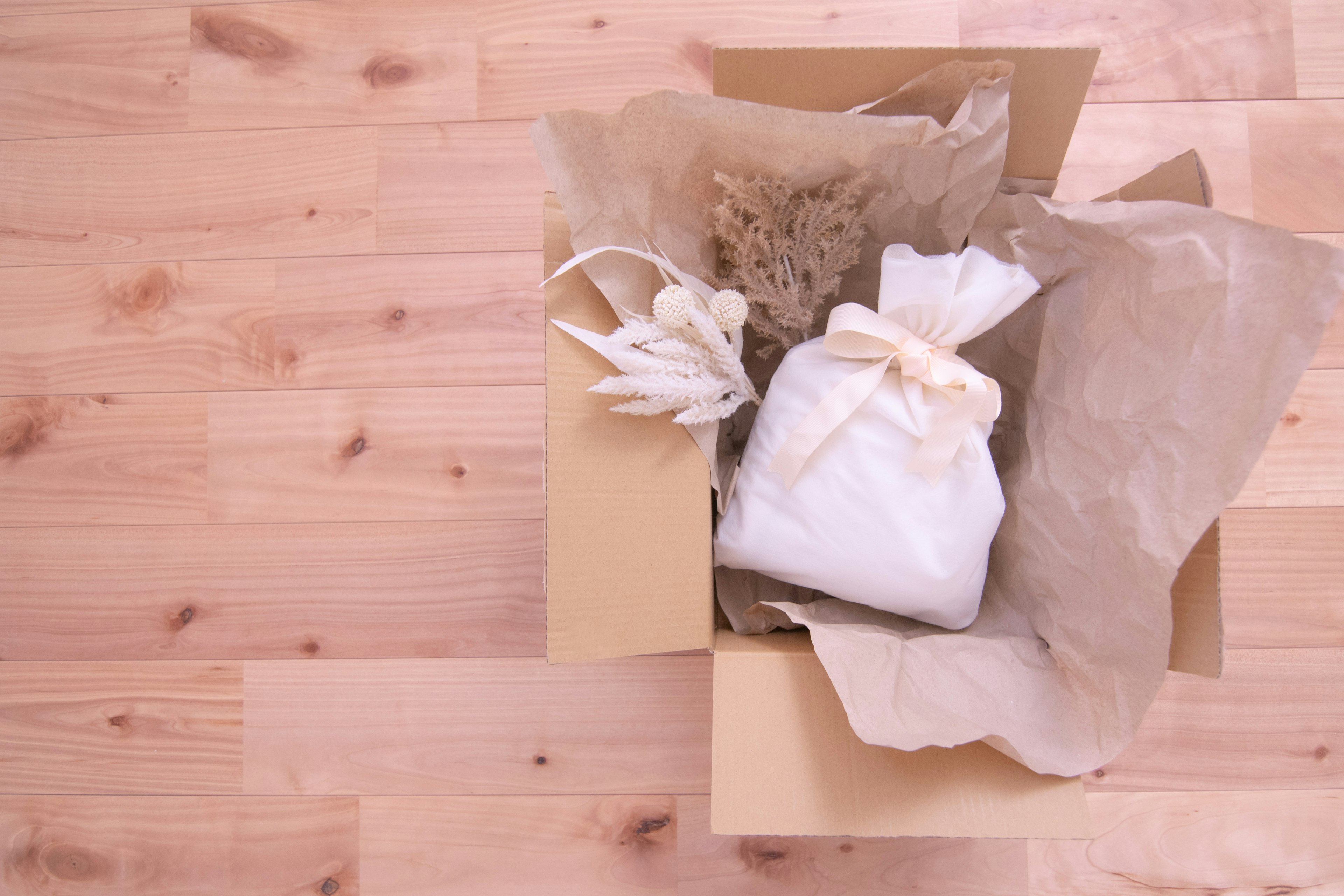 Boîte en carton ouverte contenant un sachet en tissu blanc et des fleurs séchées