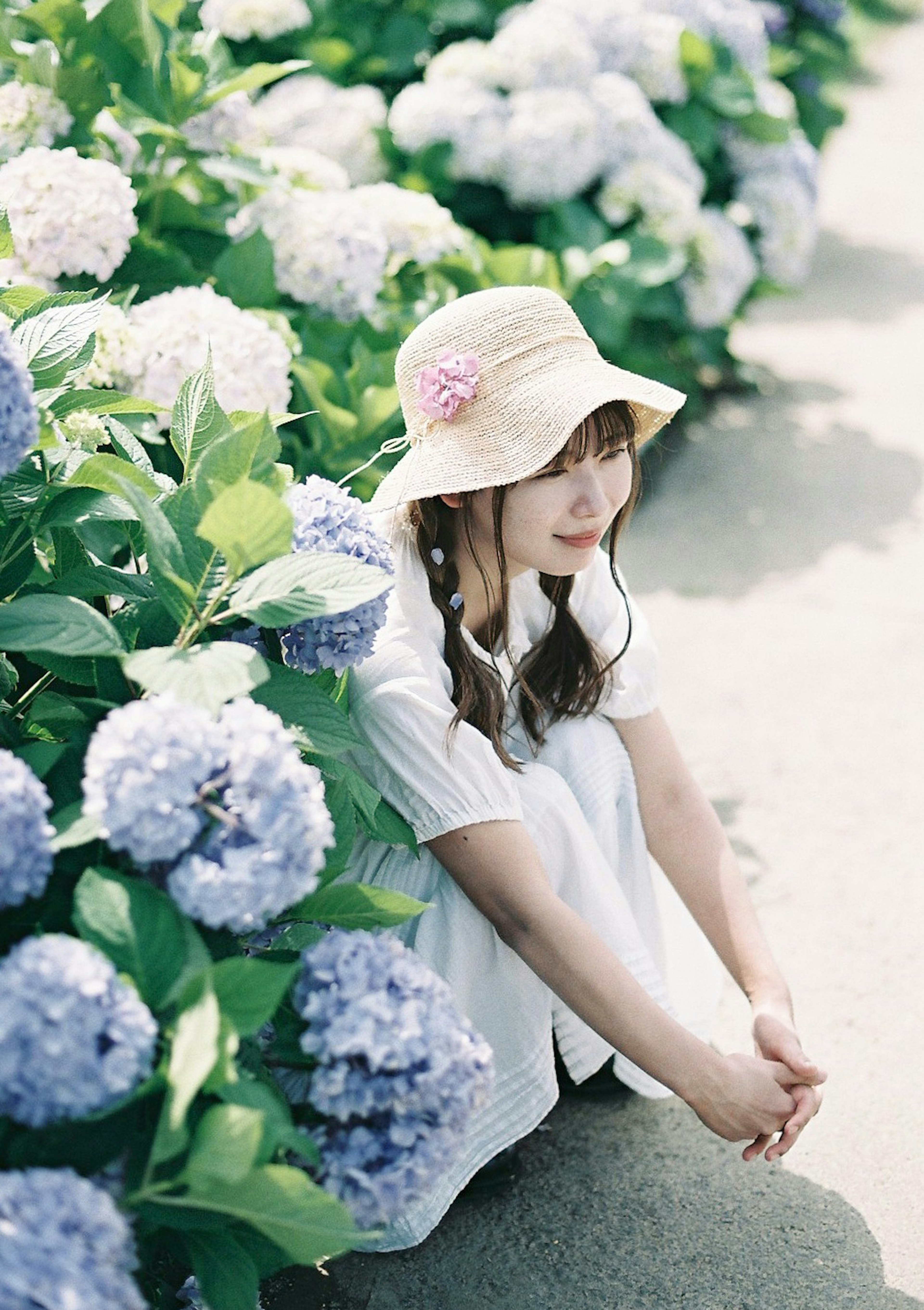 Una mujer con un vestido blanco sentada entre flores de hortensia azules