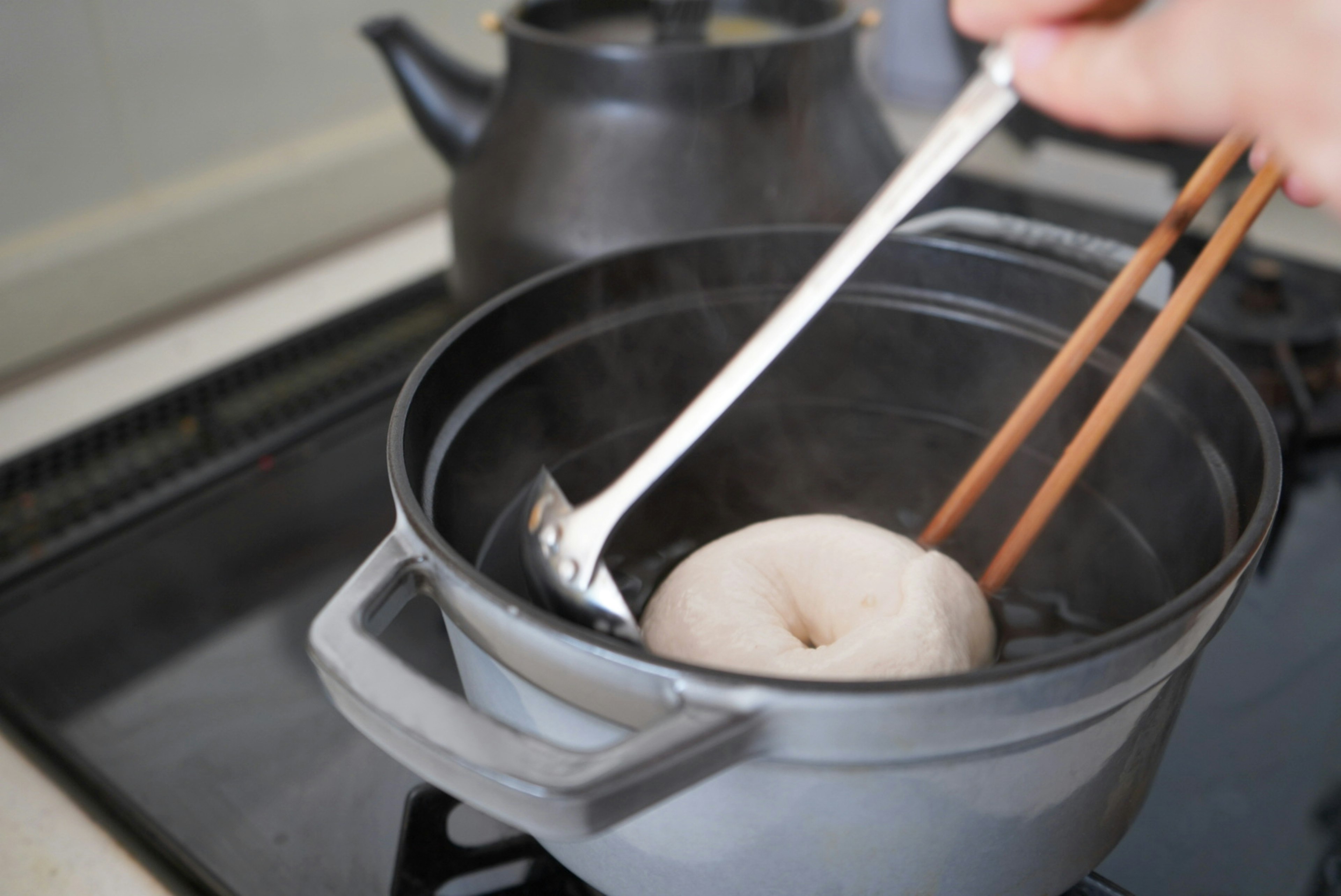 Una mano levantando un dumpling blanco con palillos de un recipiente de vapor