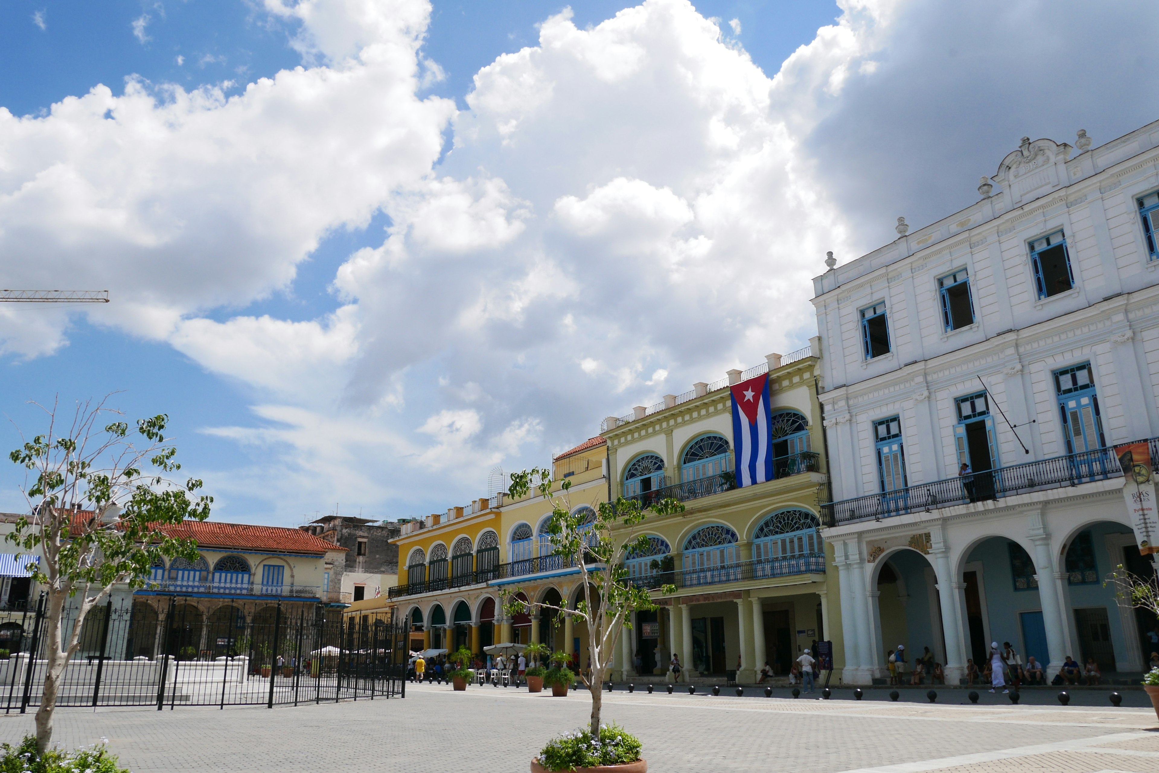 Plaza vibrante con edificios coloridos bajo un cielo brillante con la bandera cubana