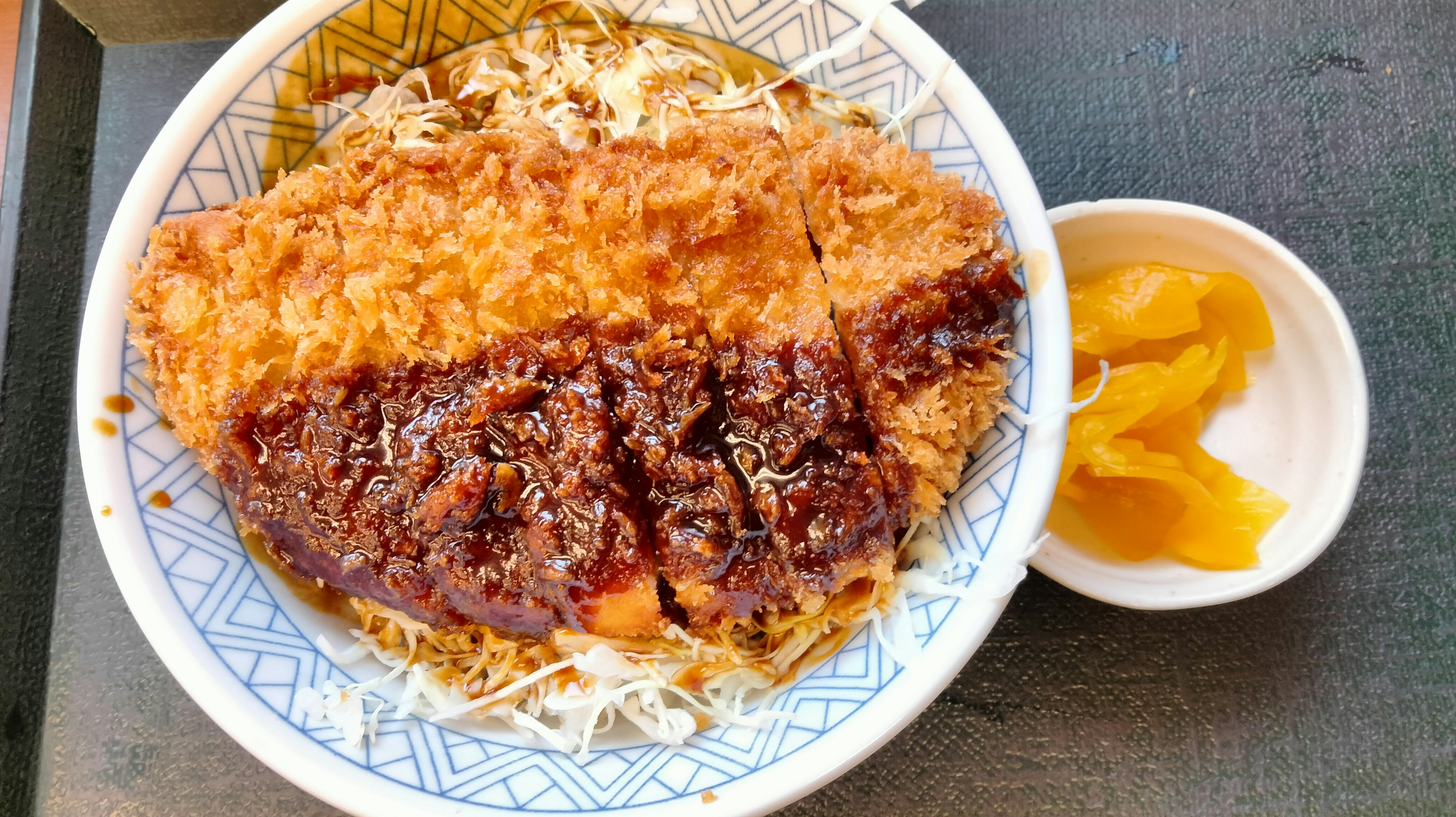 A bowl of katsu-don with shredded cabbage and pickles