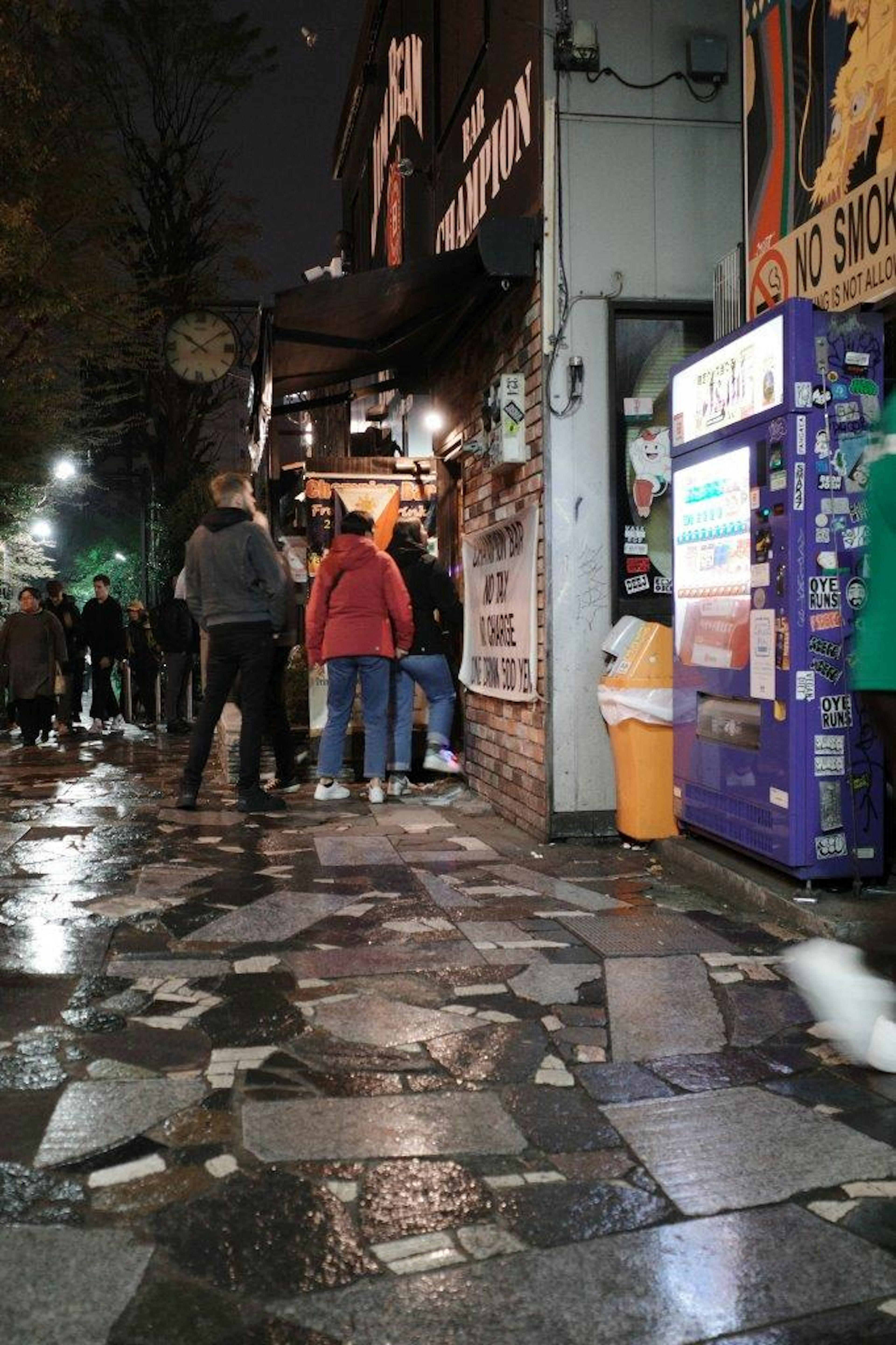 夜の街角に立つ人々と濡れた石畳の通り