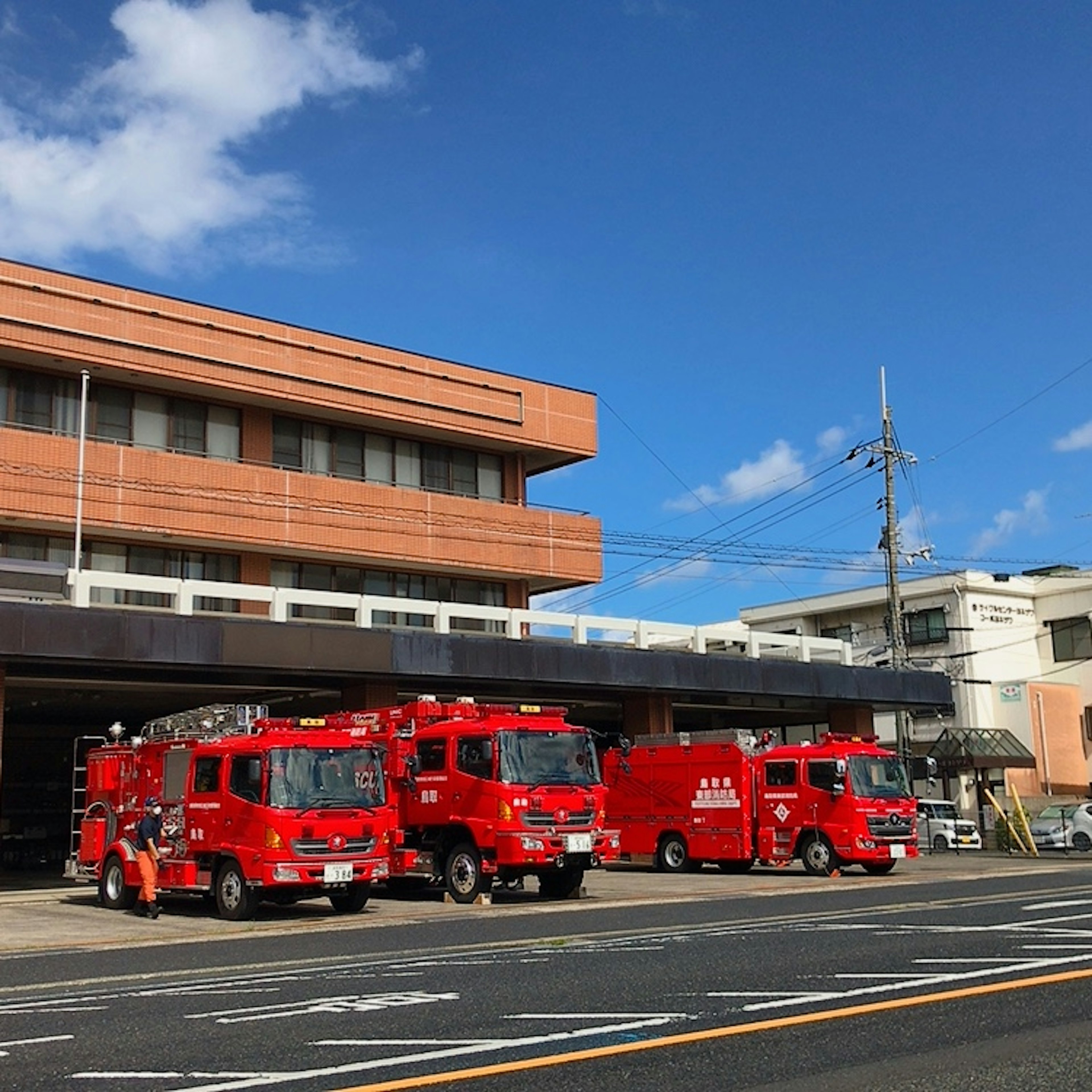 Fire station exterior with red fire trucks parked under a blue sky