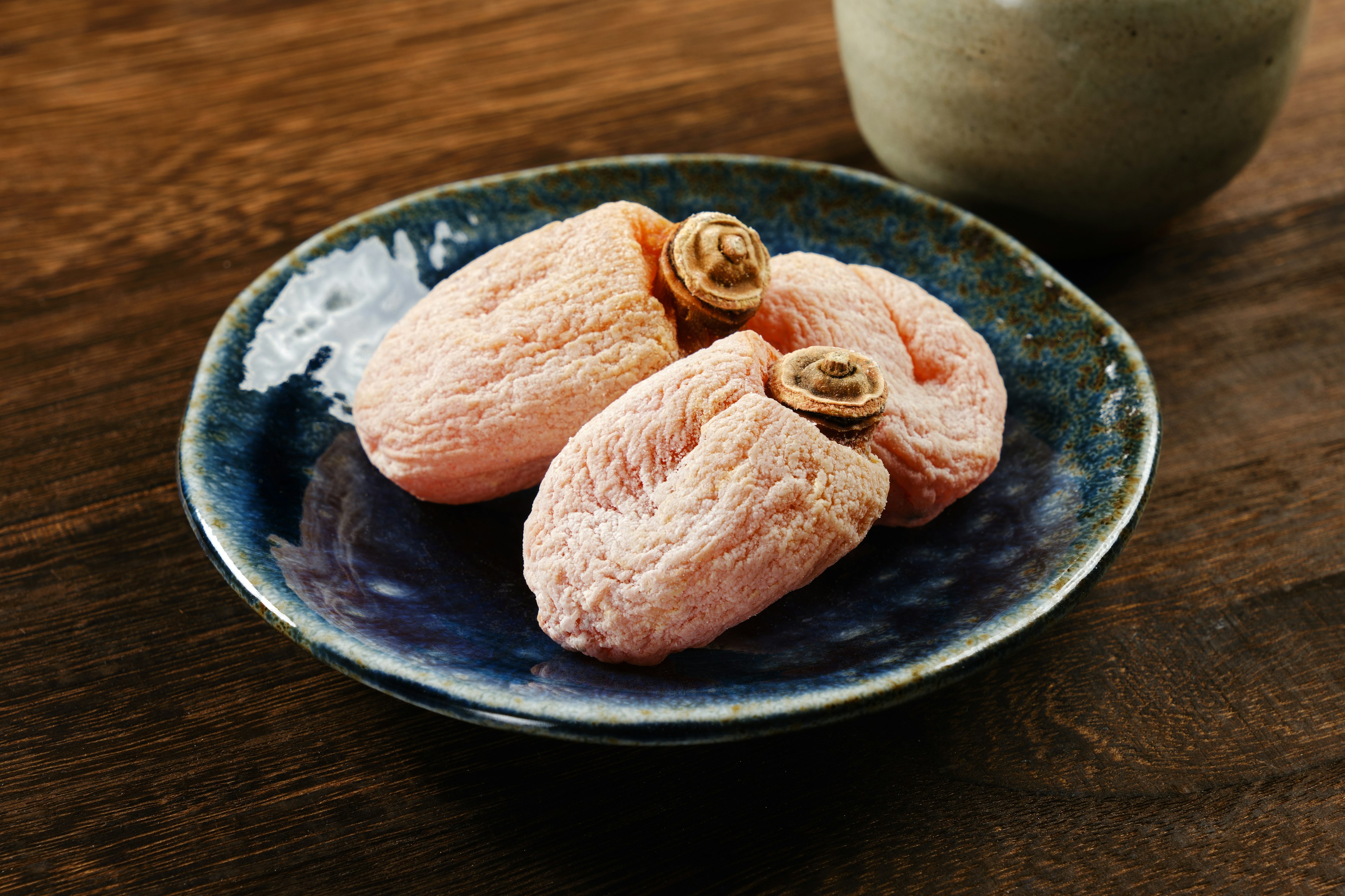 Three pink Japanese sweets on a ceramic plate with a teacup in the background