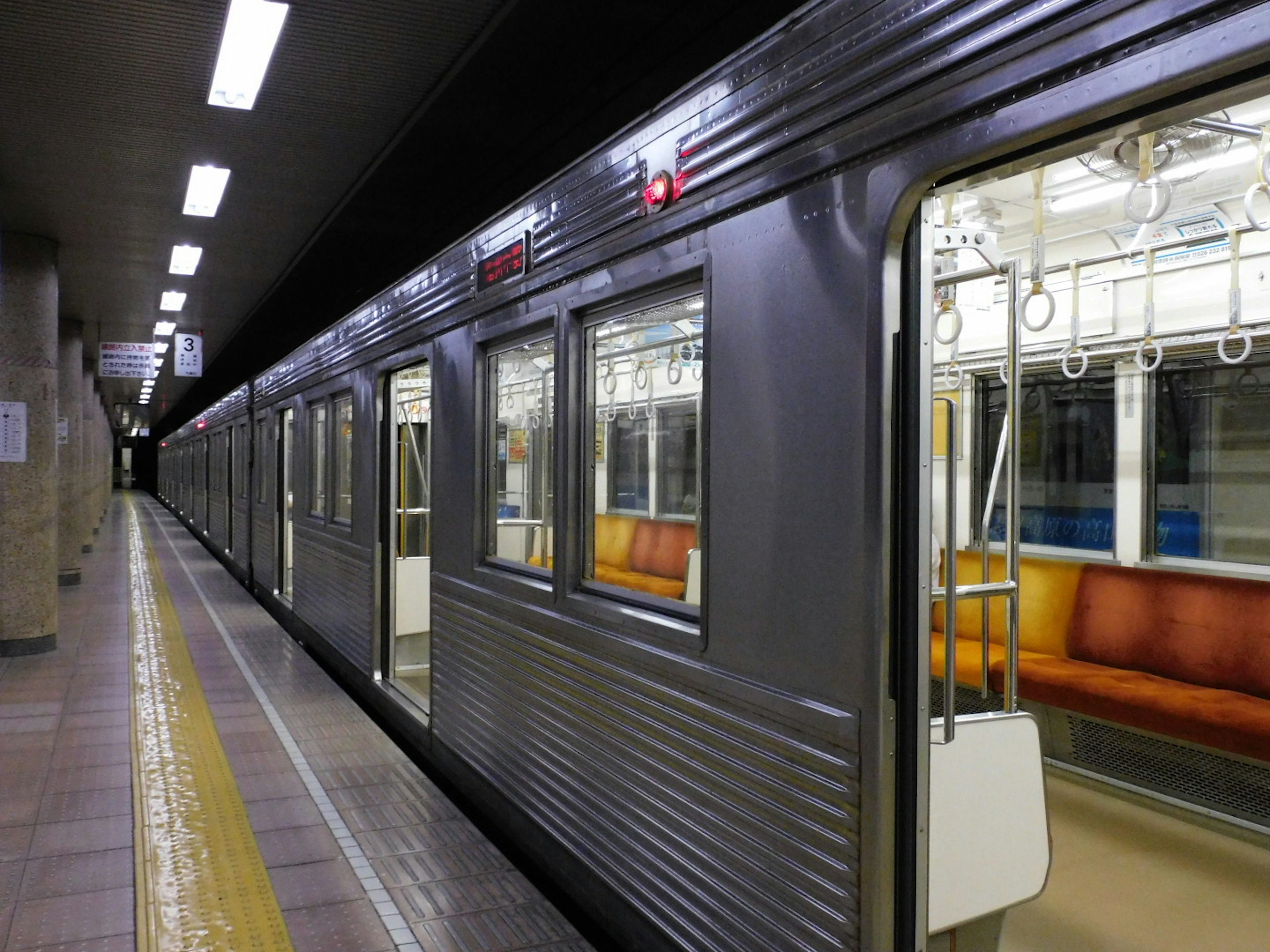 Foto kereta metro di stasiun dengan eksterior gelap dan kursi oranye