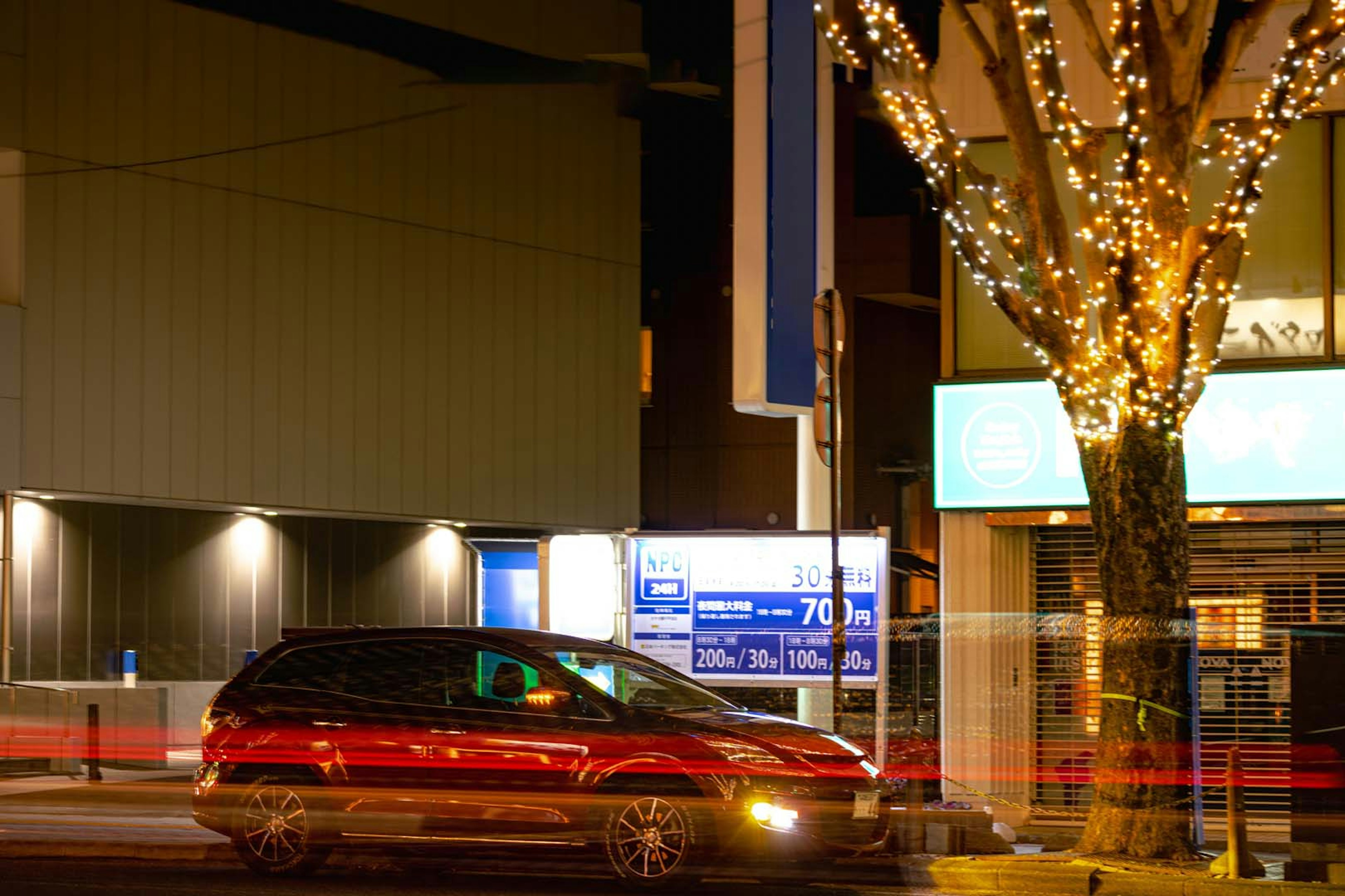 Red car parked on a city street at night with illuminated tree