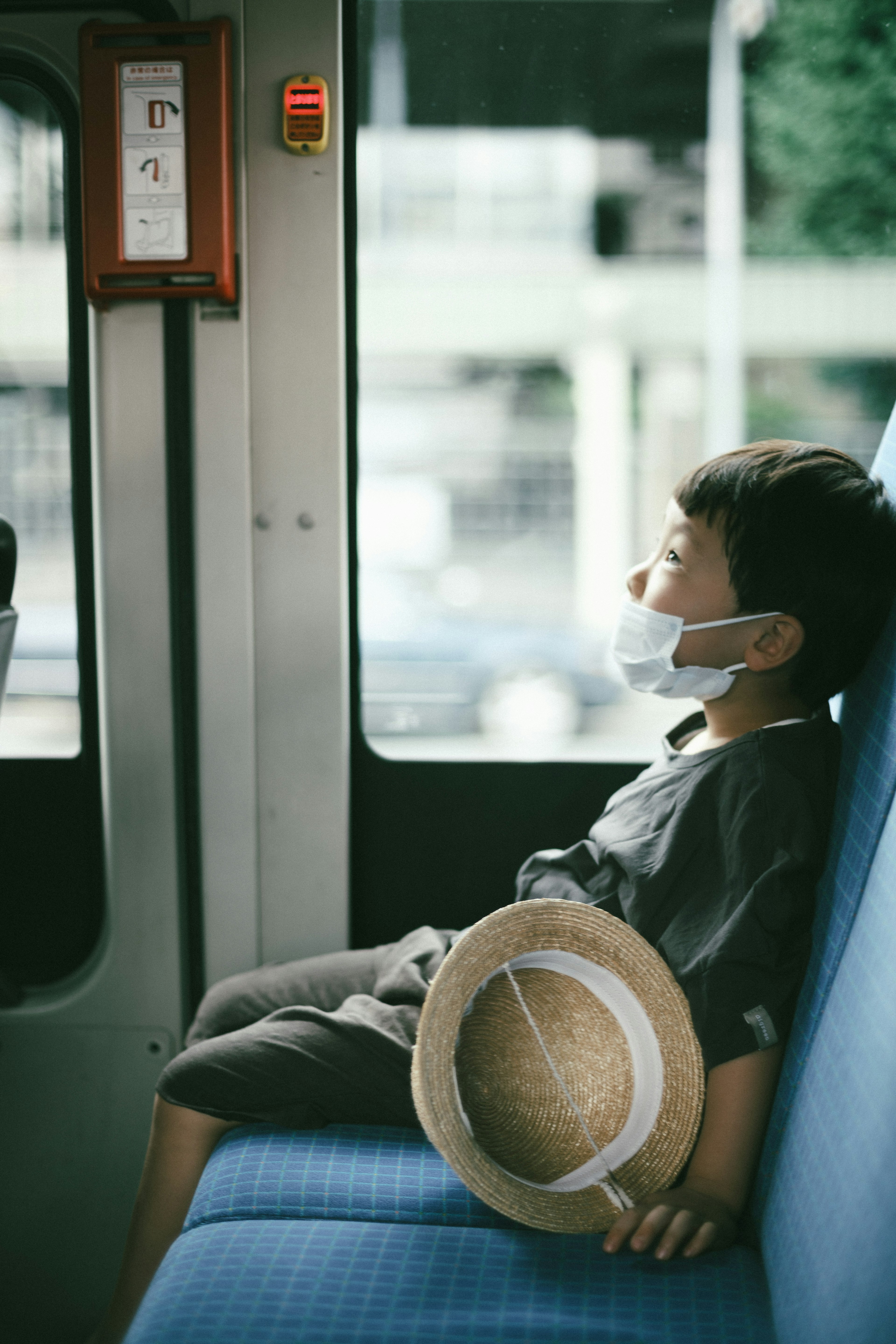 Un niño con una máscara sentado en un autobús con un sombrero de paja a su lado