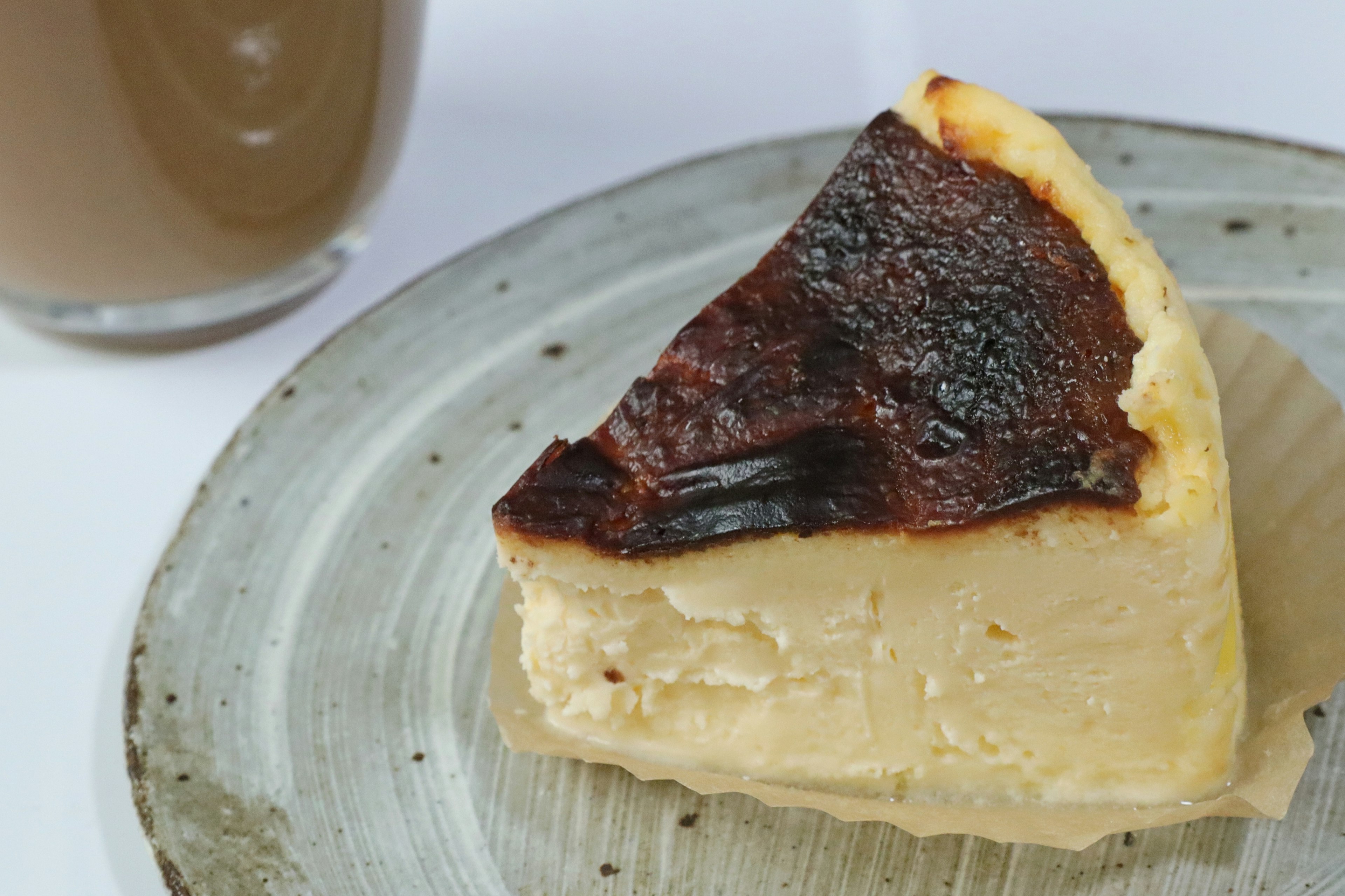 Rebanada de cheesecake quemado con una bebida al fondo