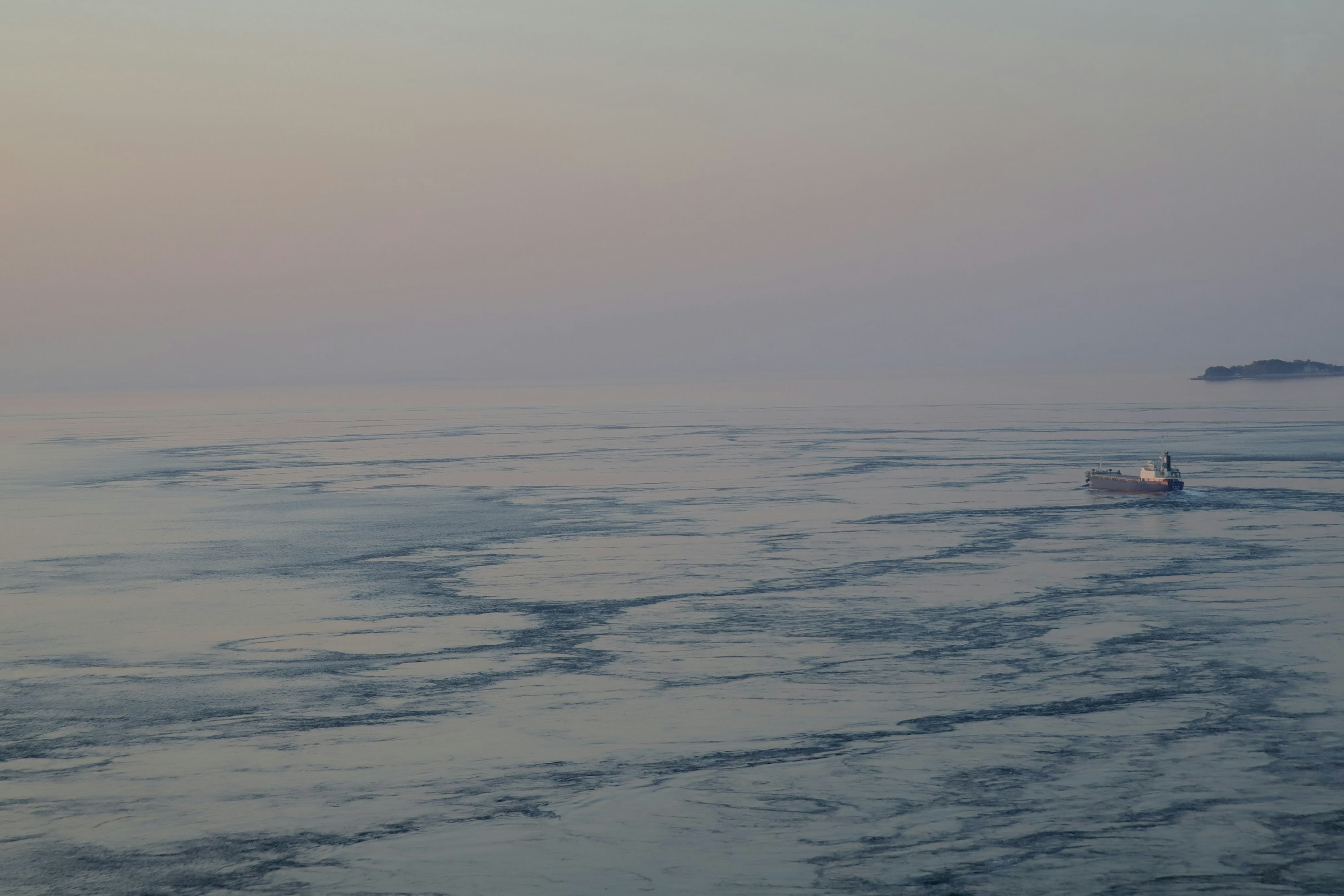 Calm sea with floating ice and a pastel sky in the background