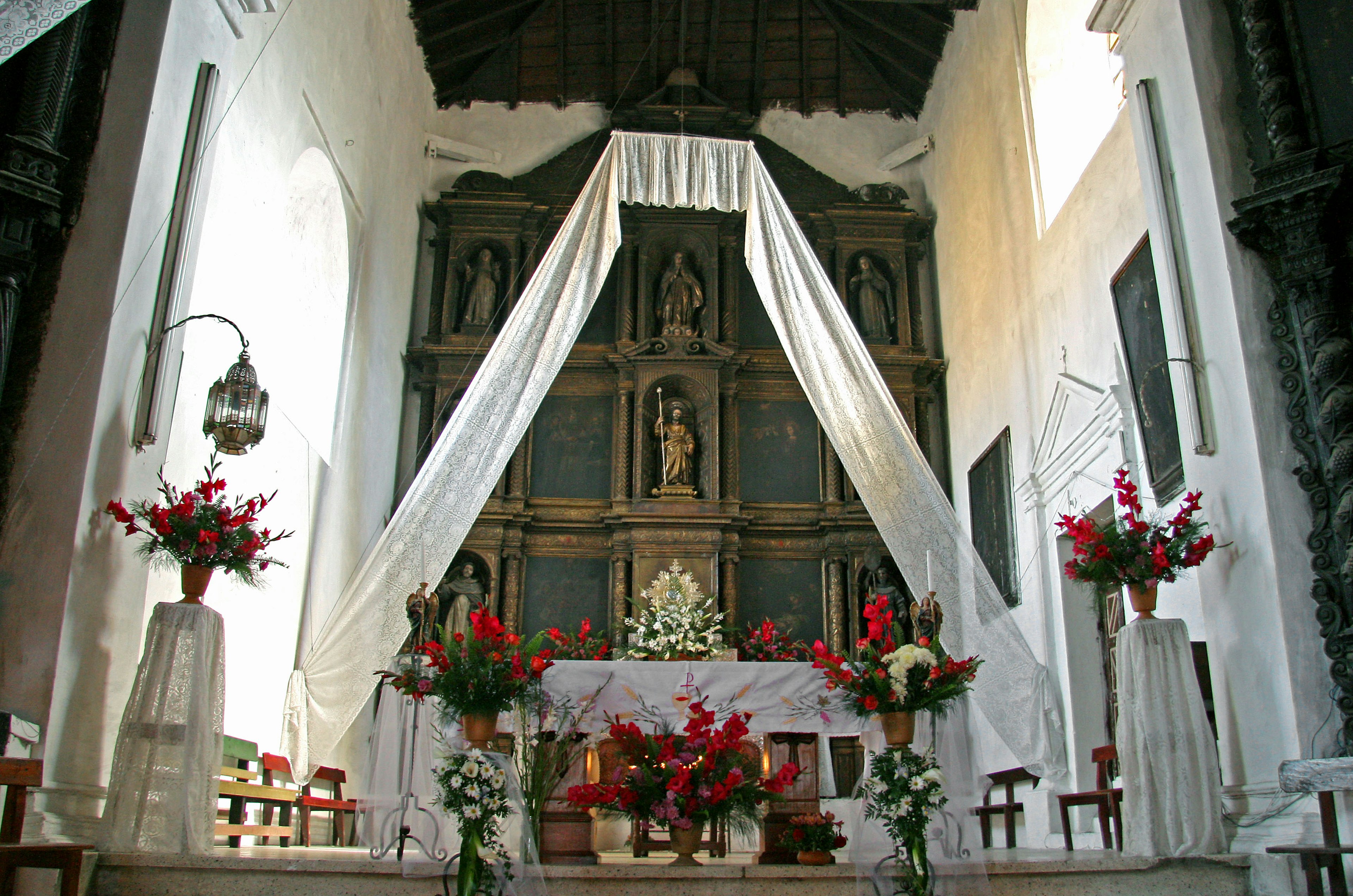 Interior de una iglesia con un hermoso altar adornado con cortinas blancas y flores rojas