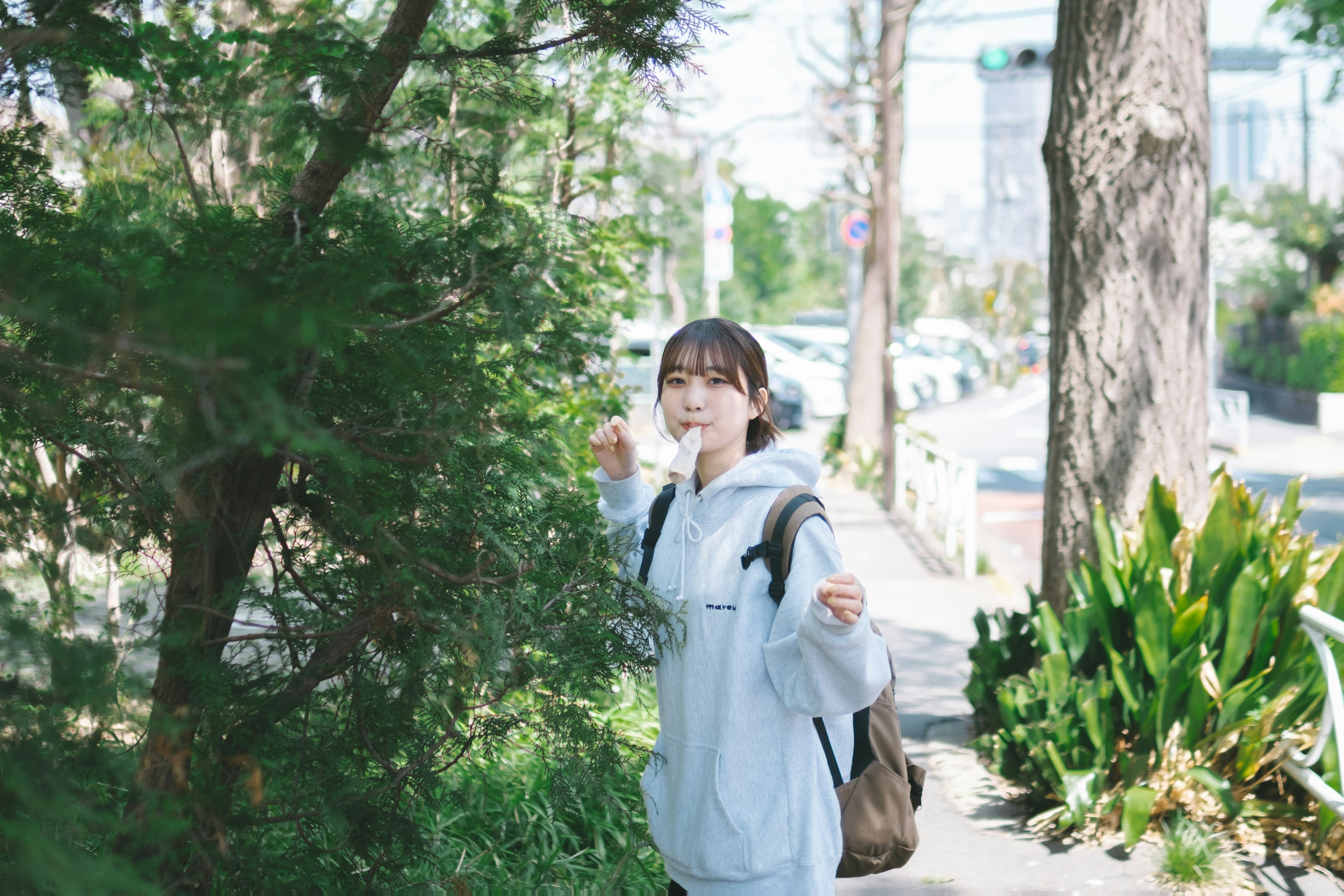 A woman in a white jacket walking near green trees