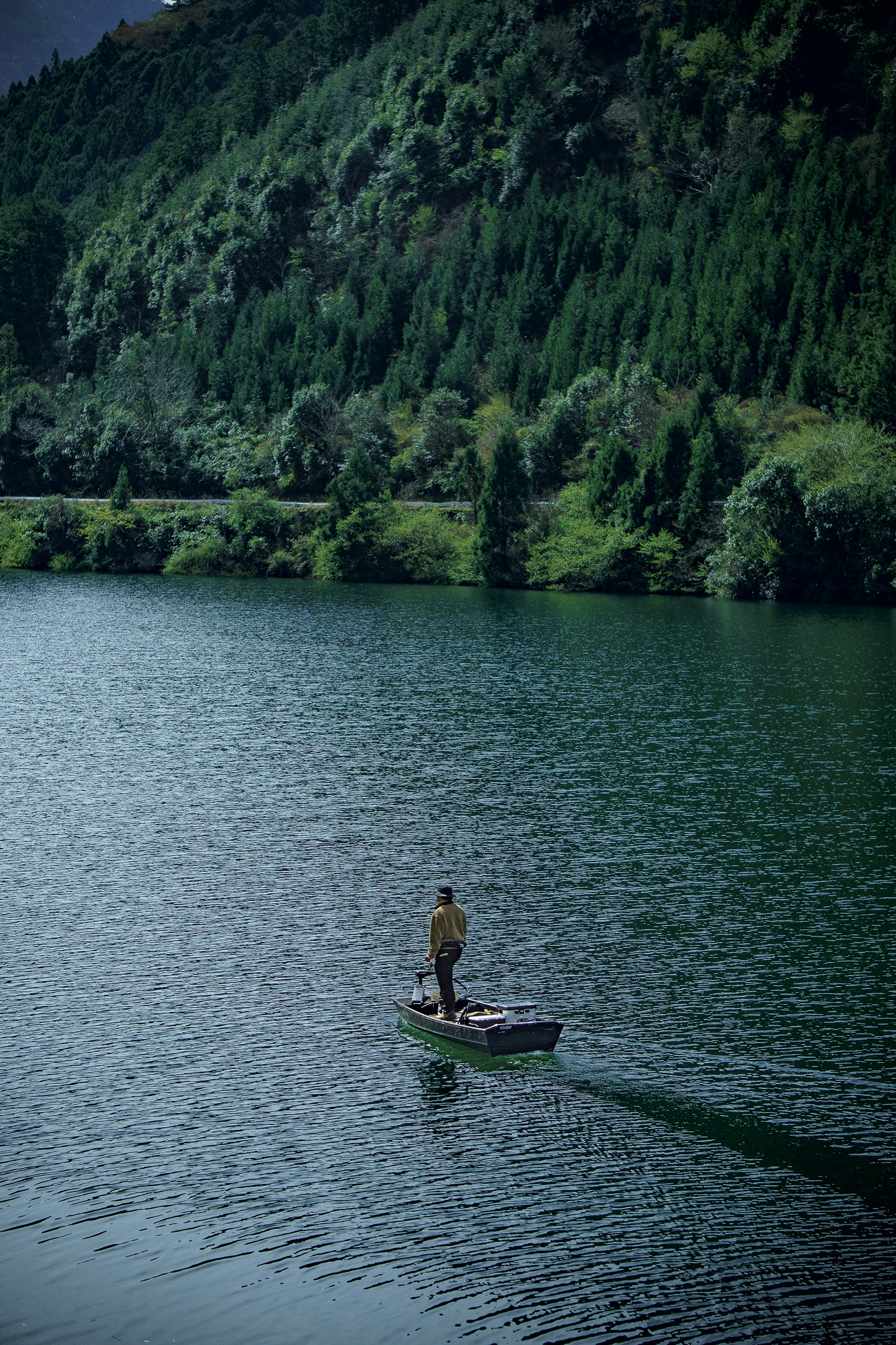 Person steht in einem kleinen Boot auf einem See, umgeben von grünen Bergen