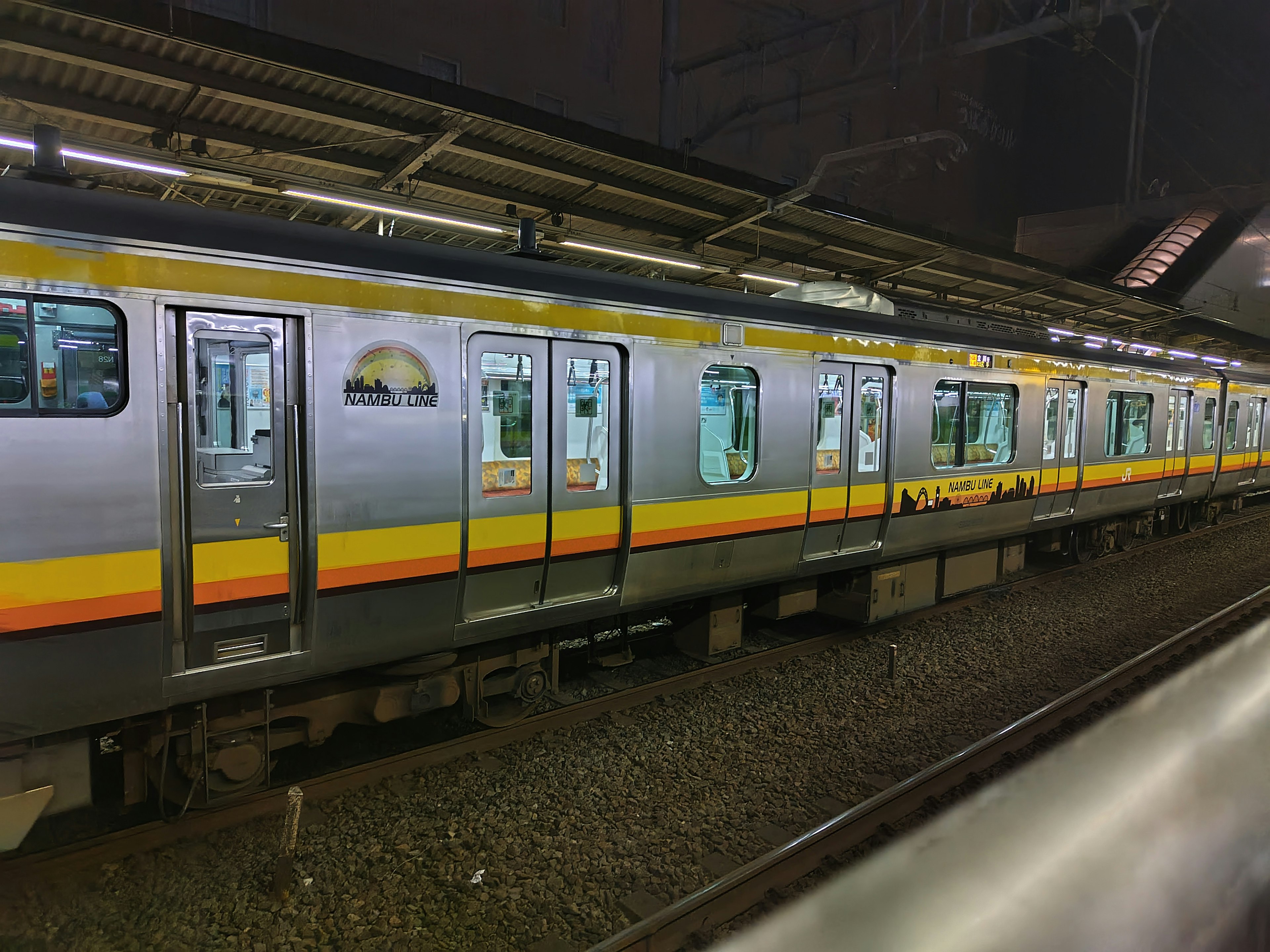 Train argenté arrêté à une station la nuit avec une bande jaune distinctive