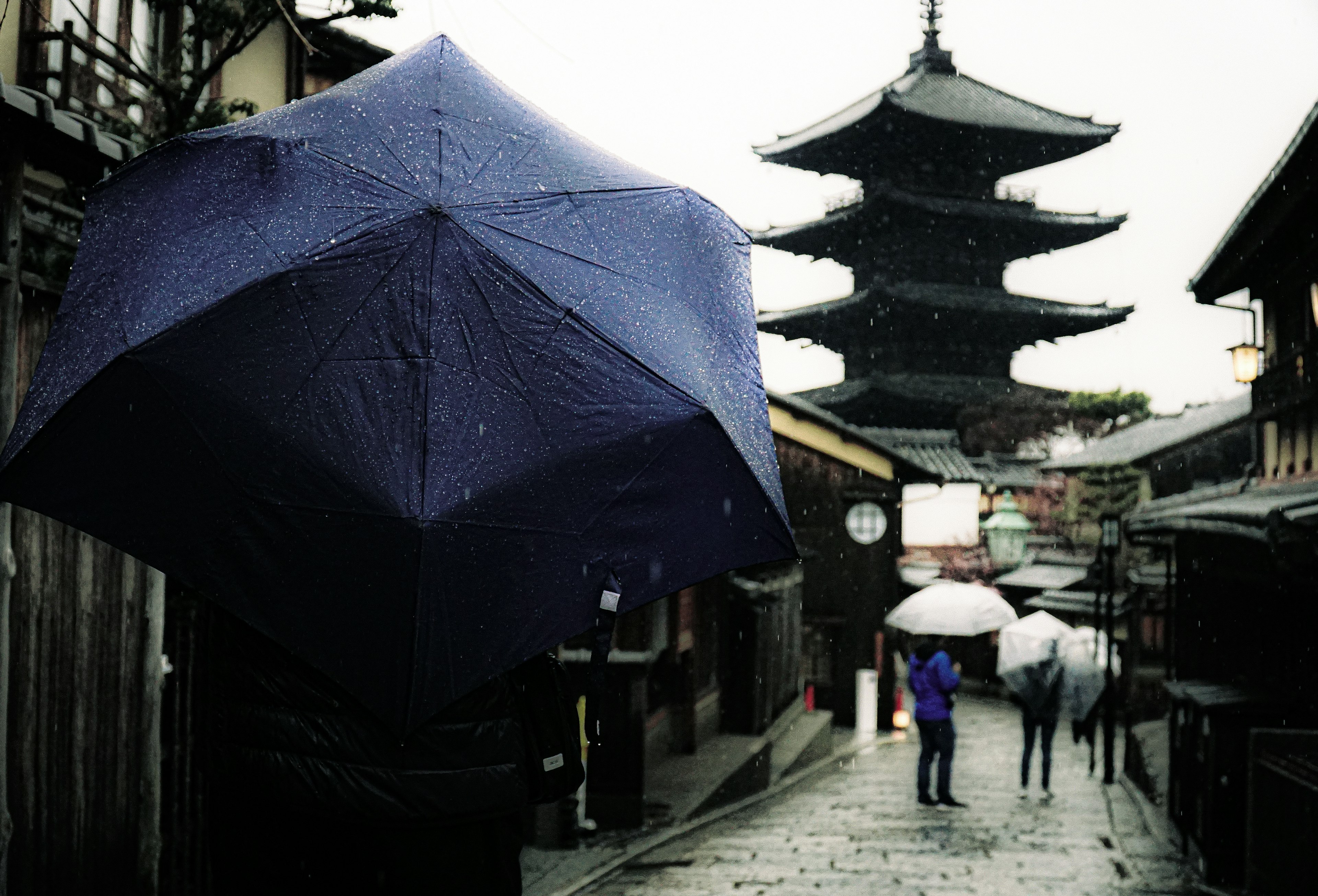 Blauer Regenschirm im Regen mit einer Pagode im Hintergrund