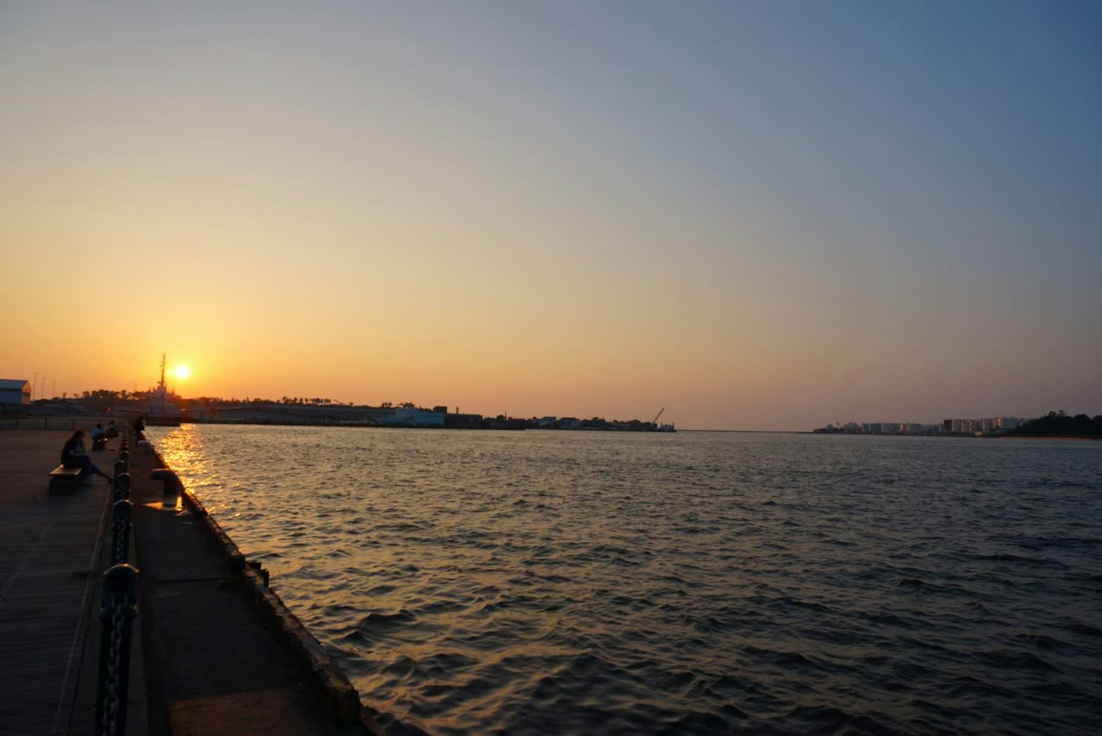 Sonnenuntergang über einem Fluss mit Silhouetten von Menschen am Ufer