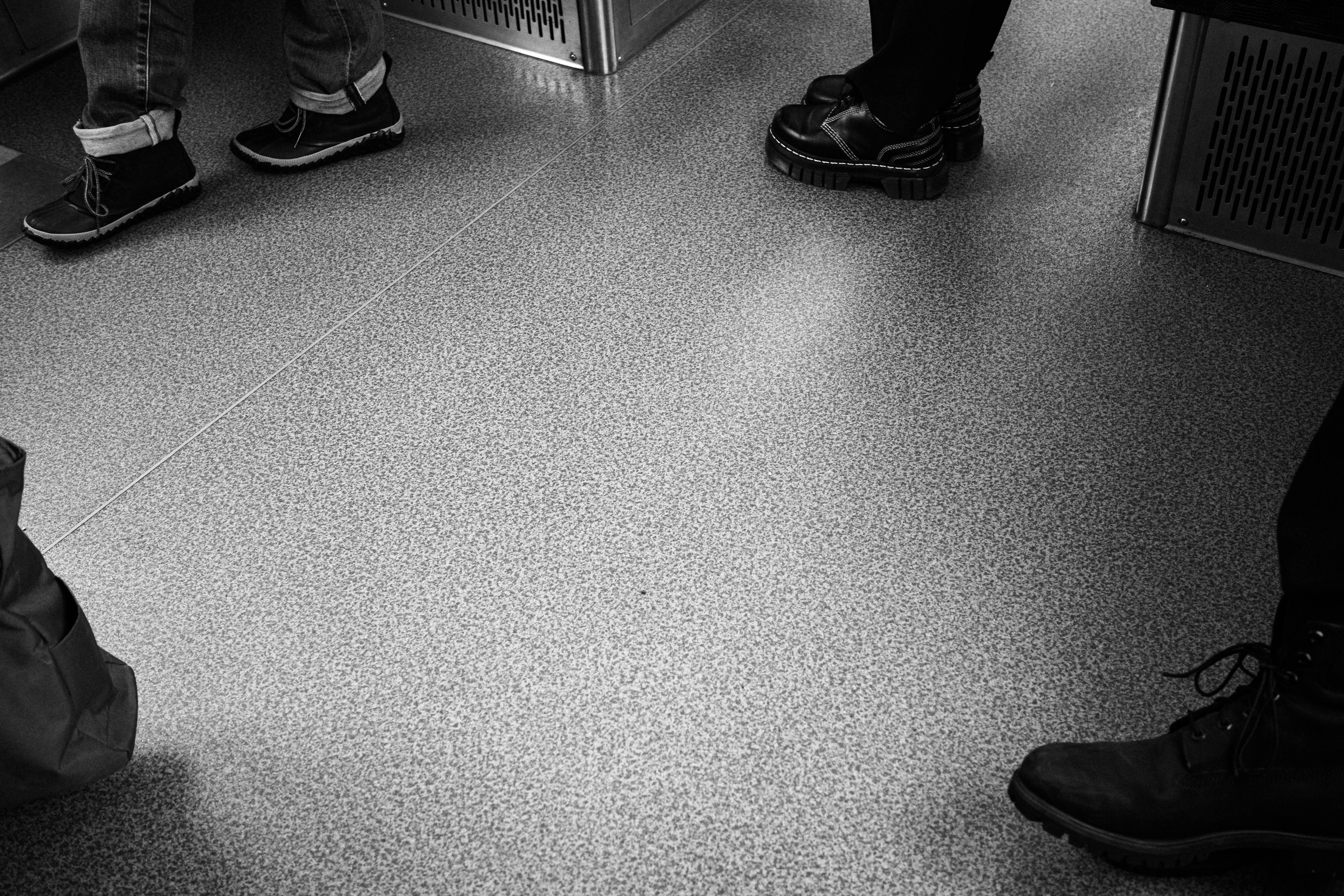 Black and white photo of feet standing on subway floor