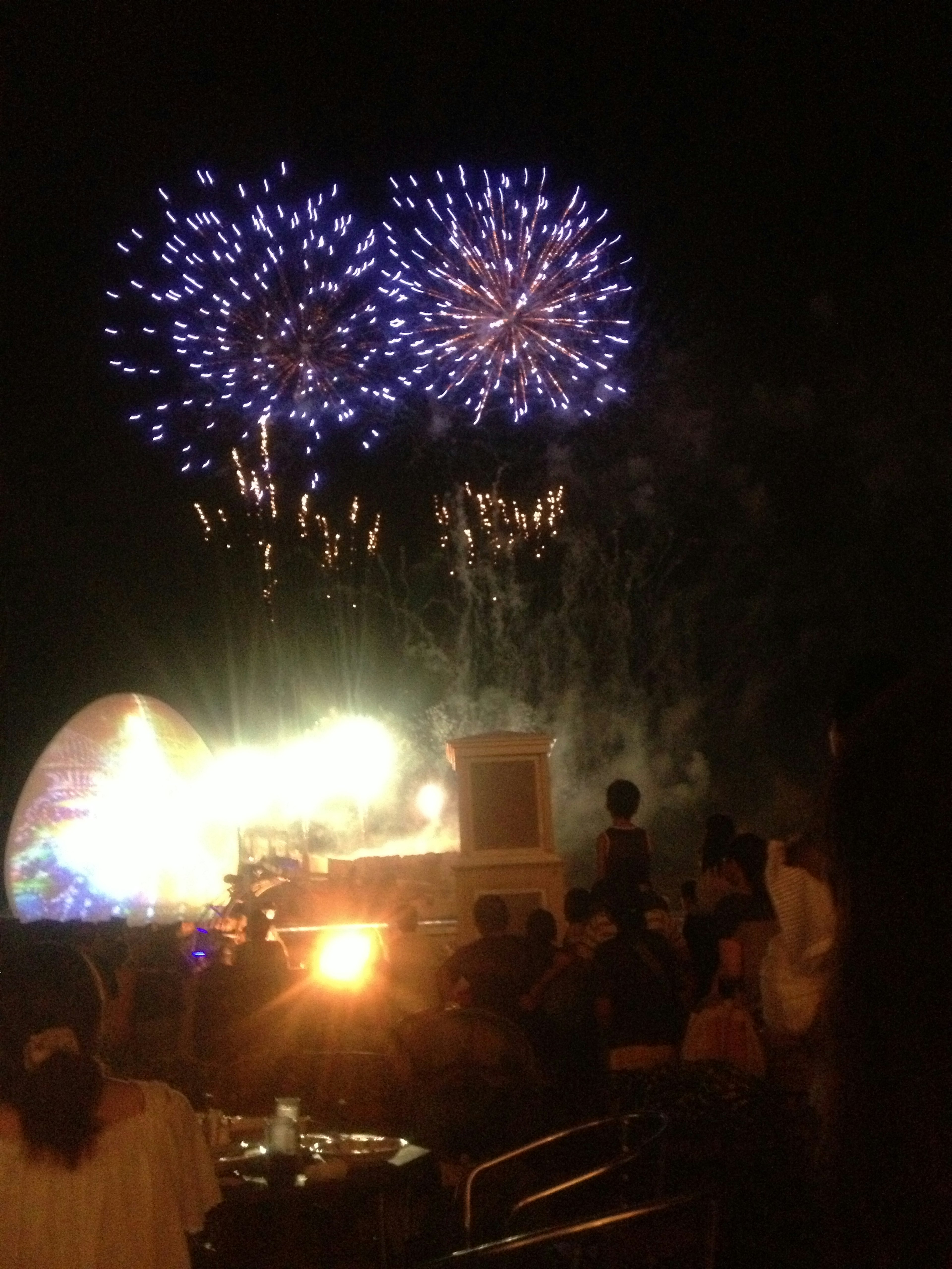 Fuegos artificiales estallando en el cielo nocturno con siluetas de espectadores