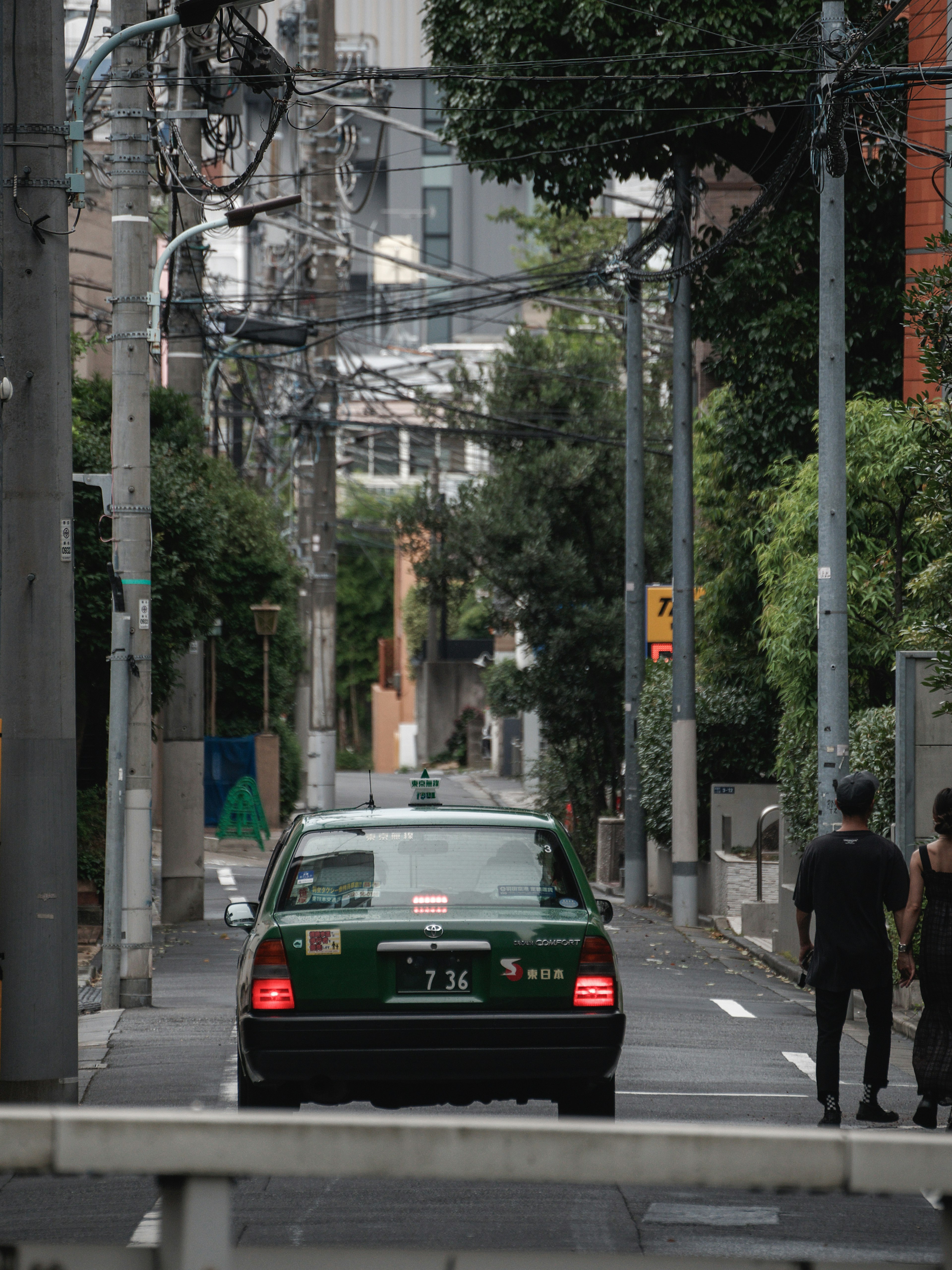 A green taxi driving down a narrow alley with pedestrians