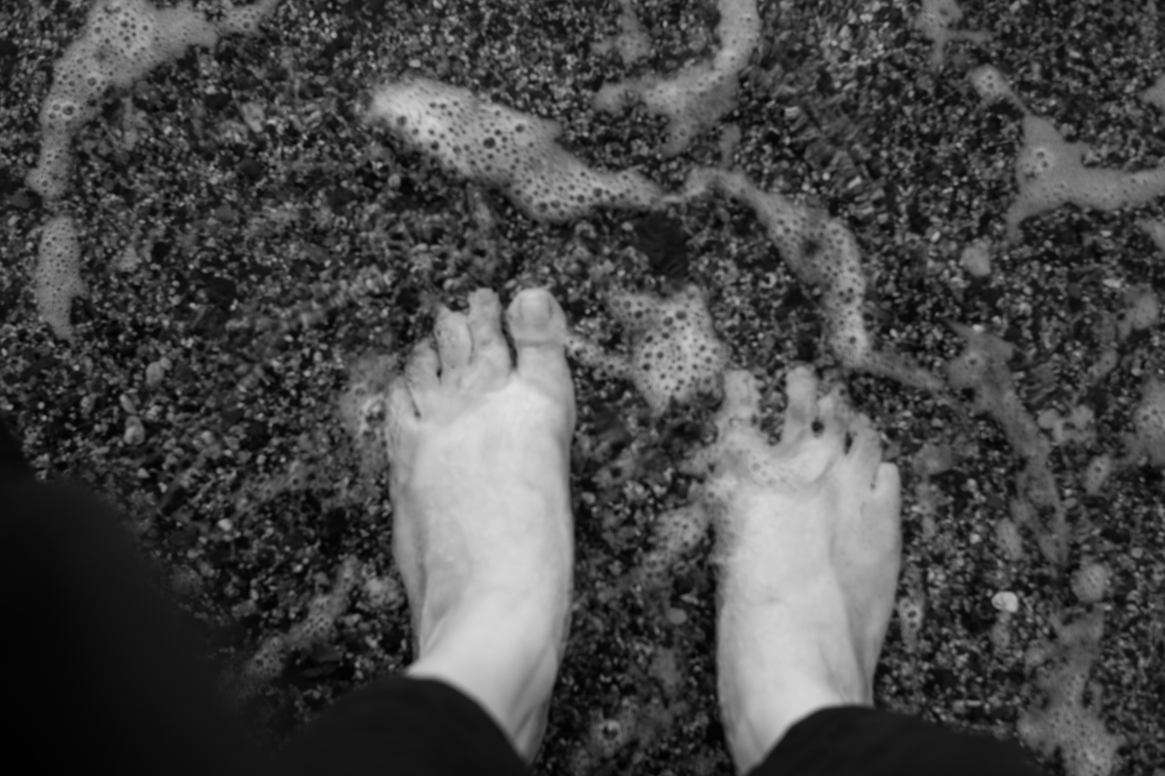 Bare feet standing on a sandy beach with foam