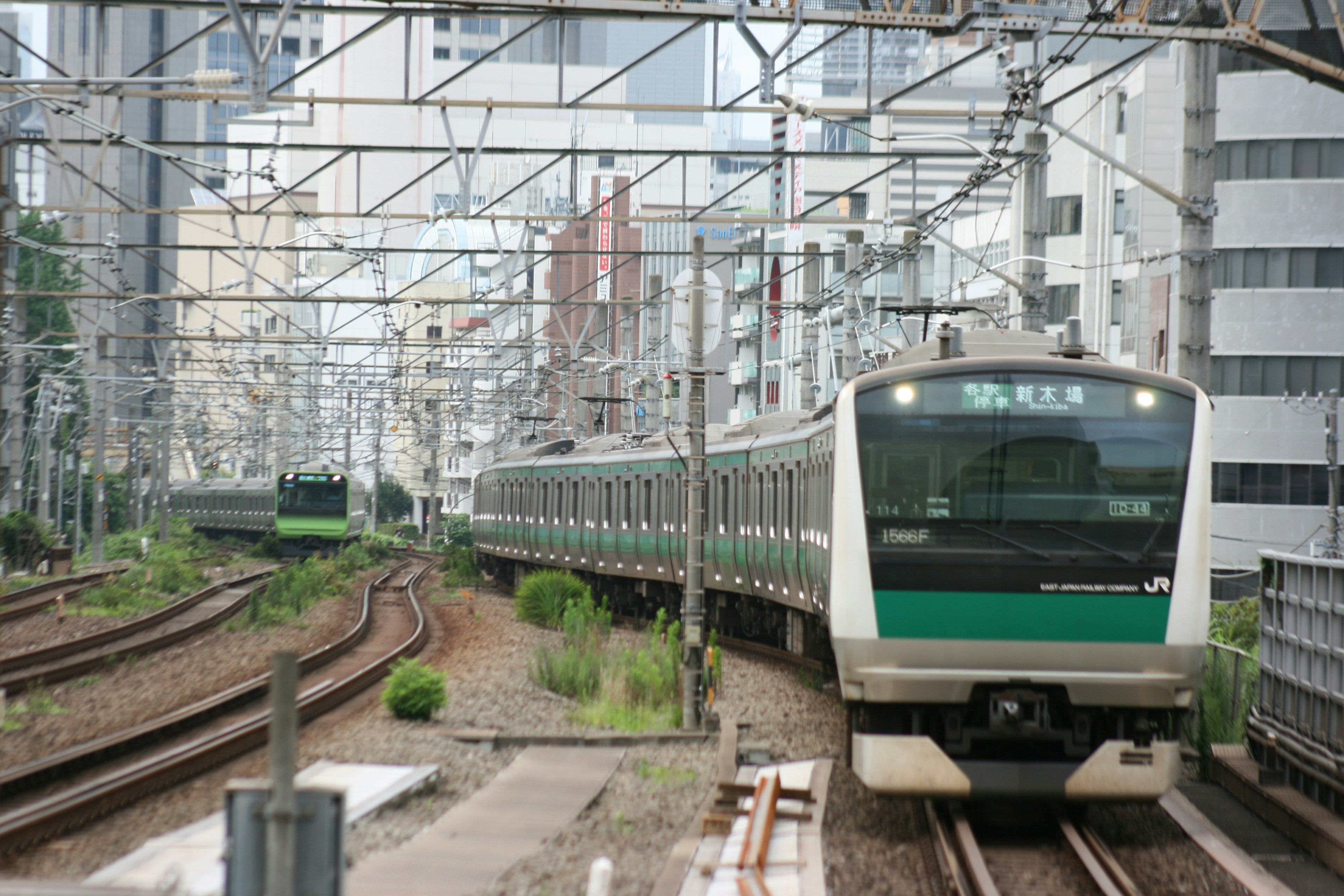 Green train navigating urban tracks surrounded by buildings