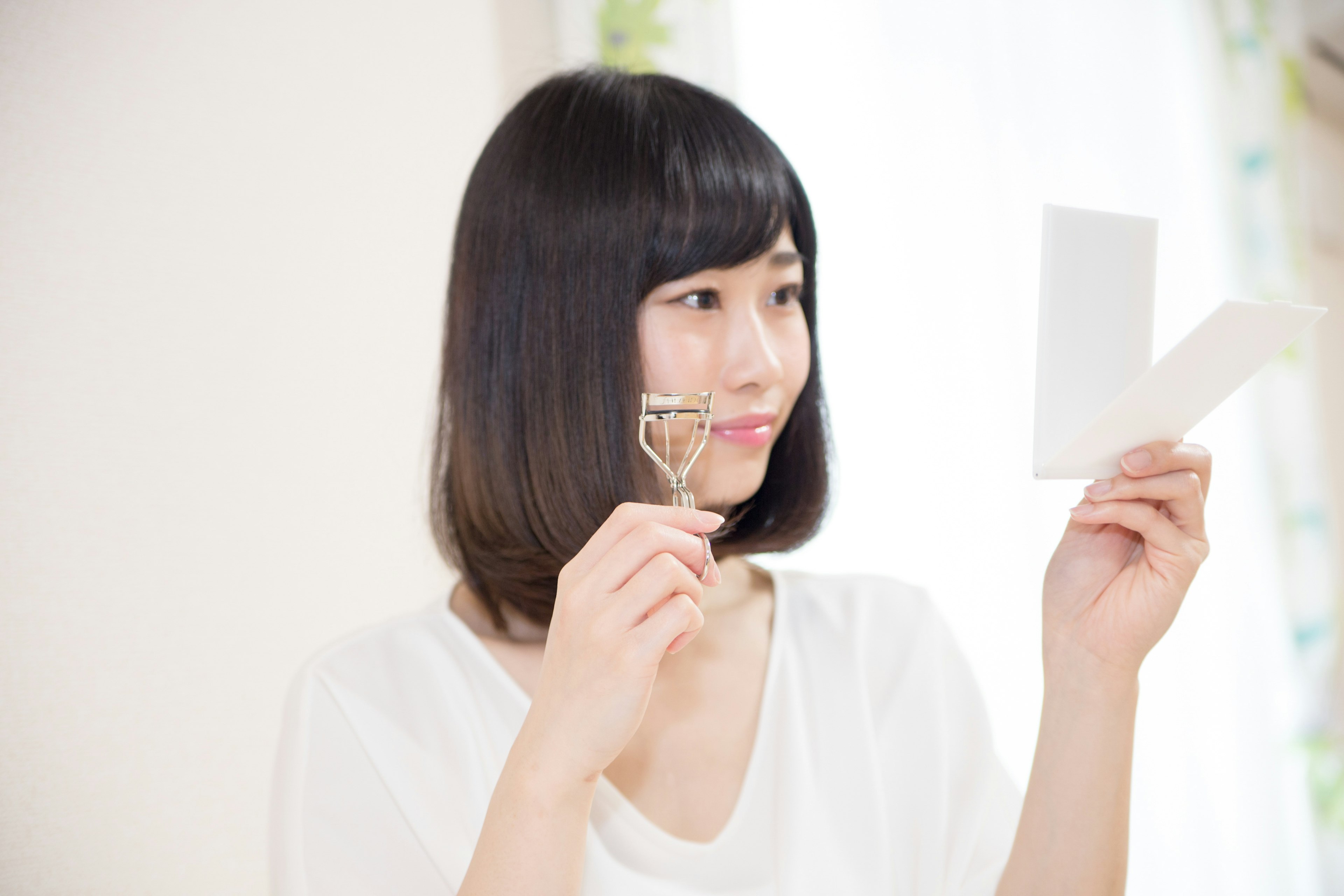 Woman holding eyelash curler while looking at a piece of paper