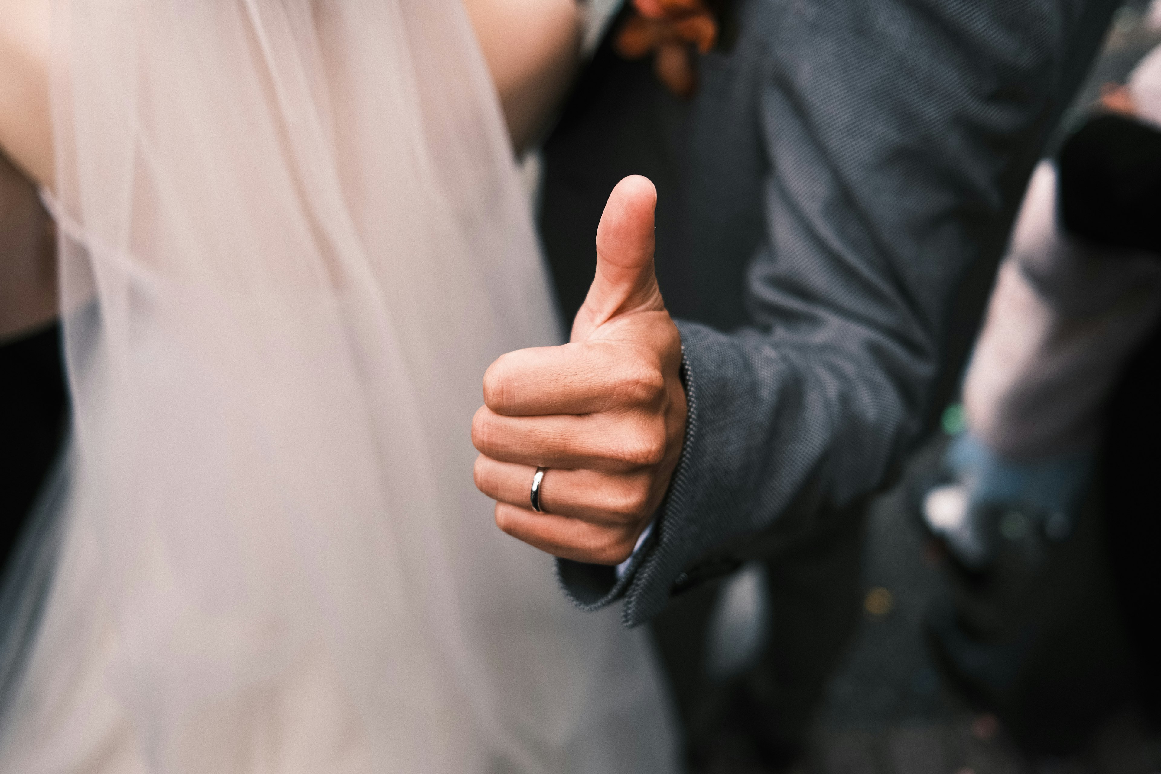 Nahaufnahme einer Hand, die beim Hochzeitsfeiern einen Daumen hoch zeigt, mit sichtbarem Ring