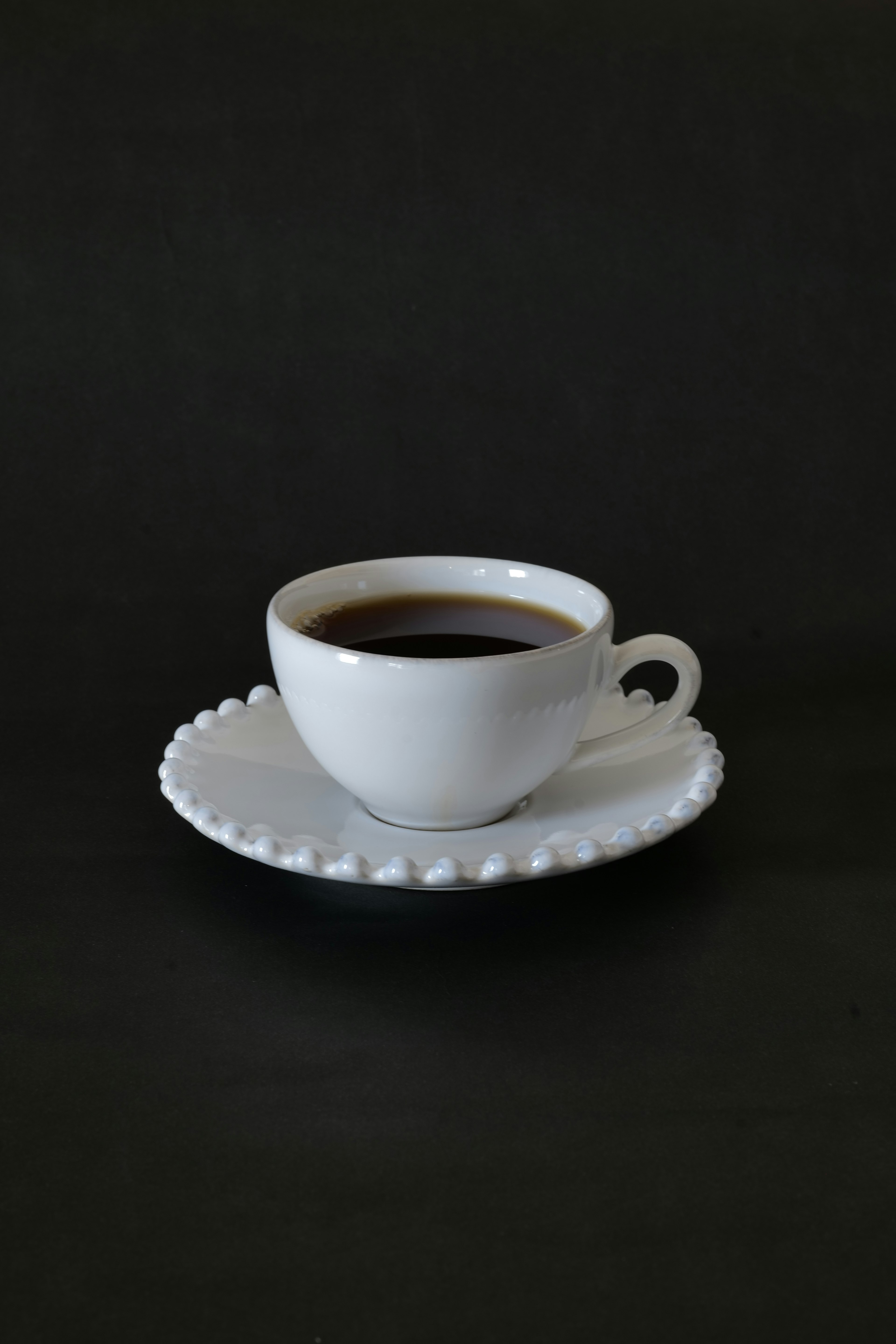 Taza de café blanca en un platillo decorativo sobre fondo negro