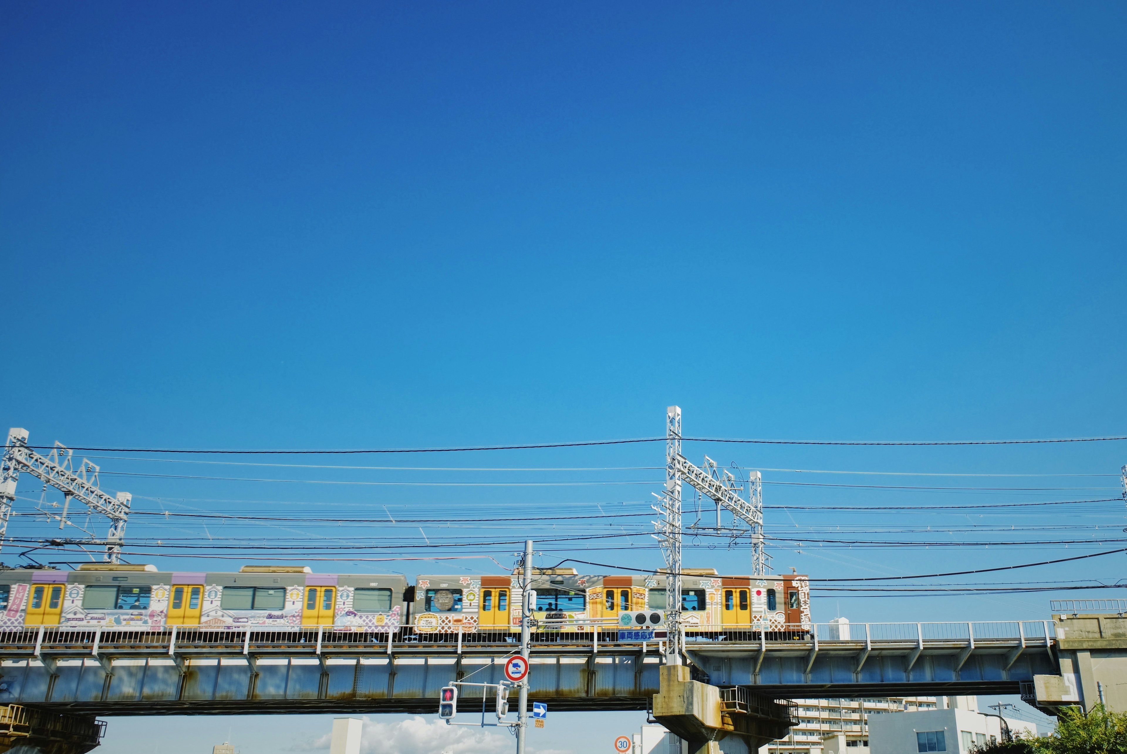 青空の下を走る黄色い電車が架線の上を移動している風景