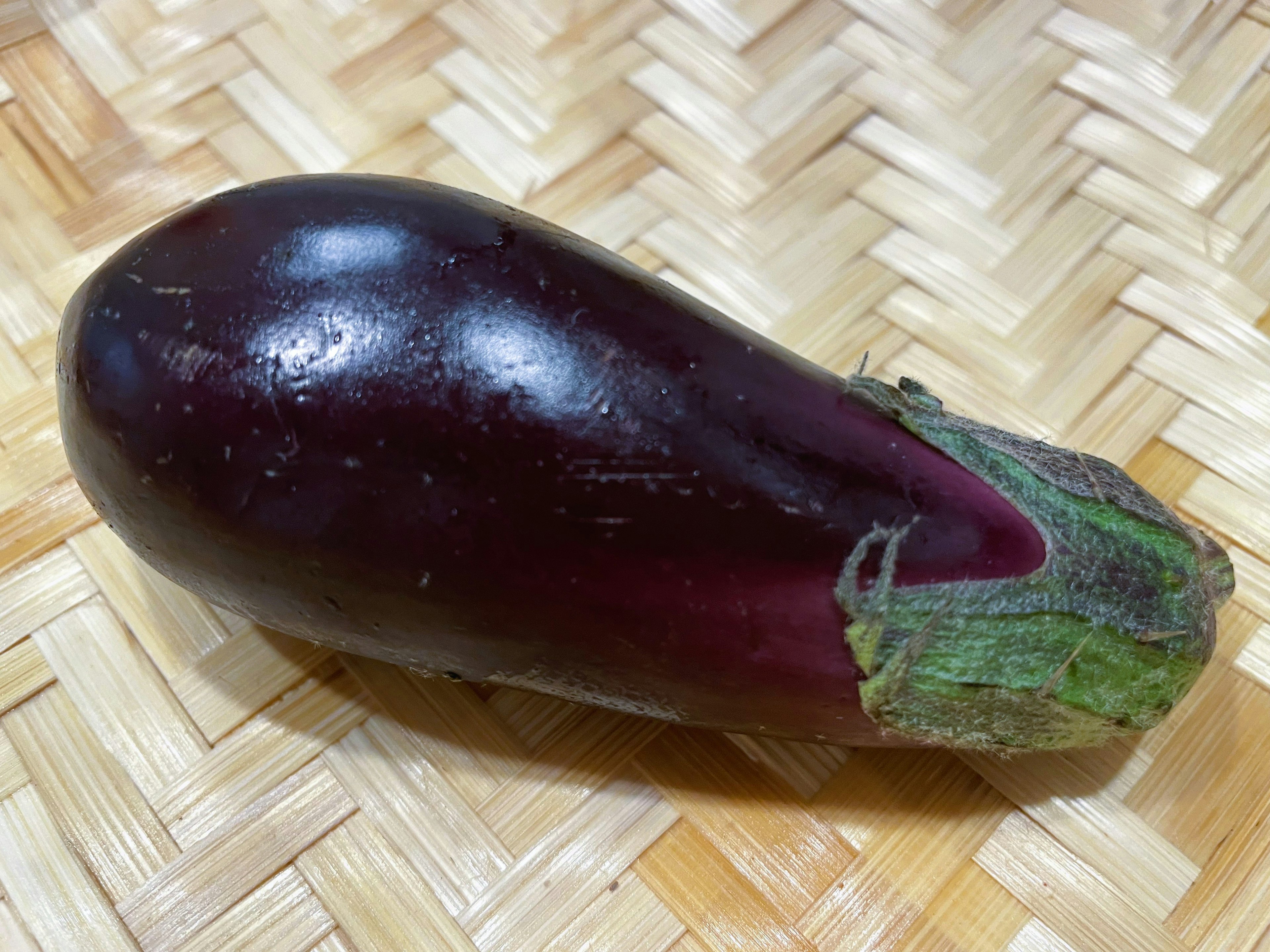 A shiny purple eggplant resting on a woven bamboo surface