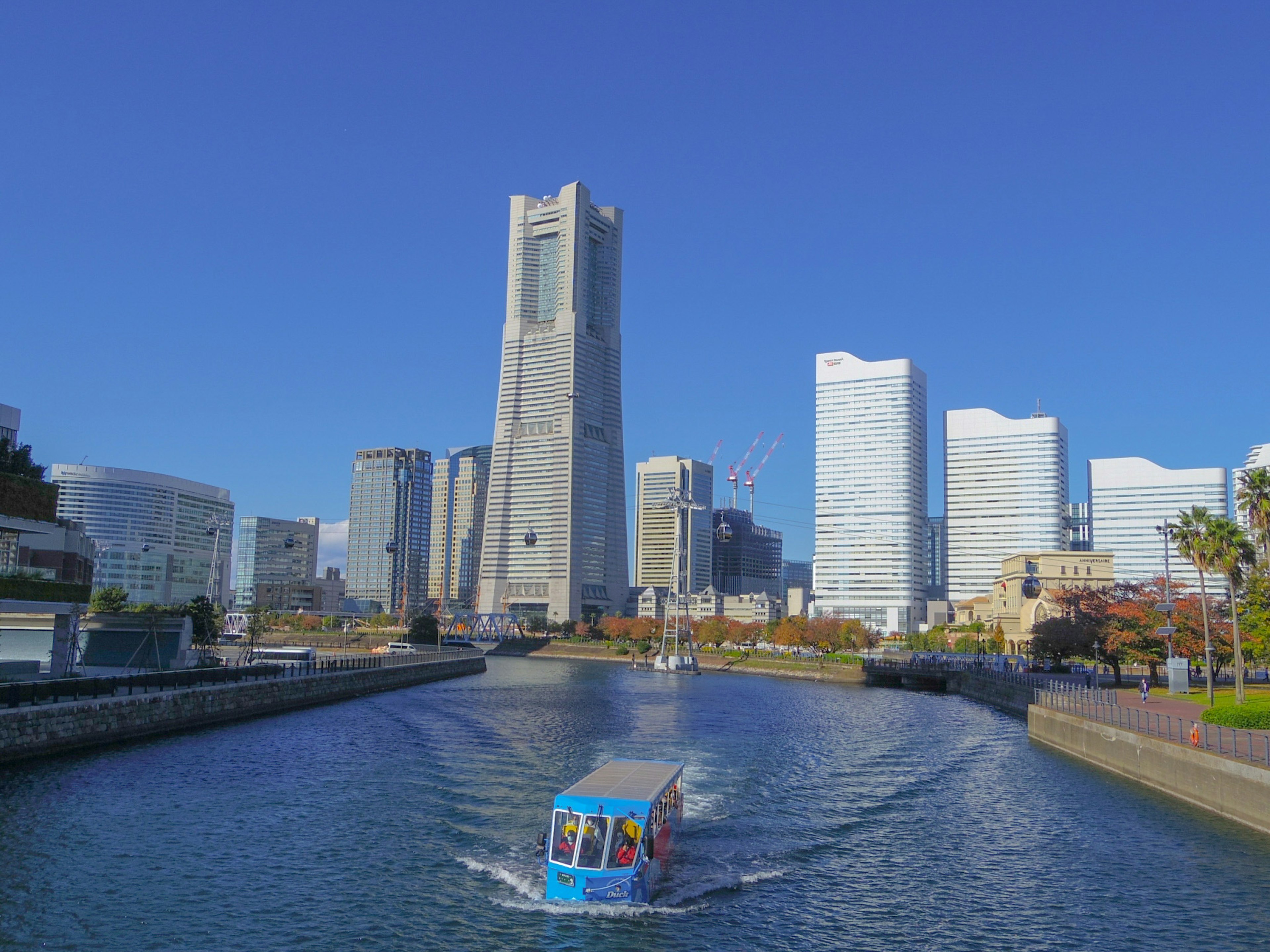 A boat navigating a canal with Yokohama Landmark Tower and modern buildings in the background