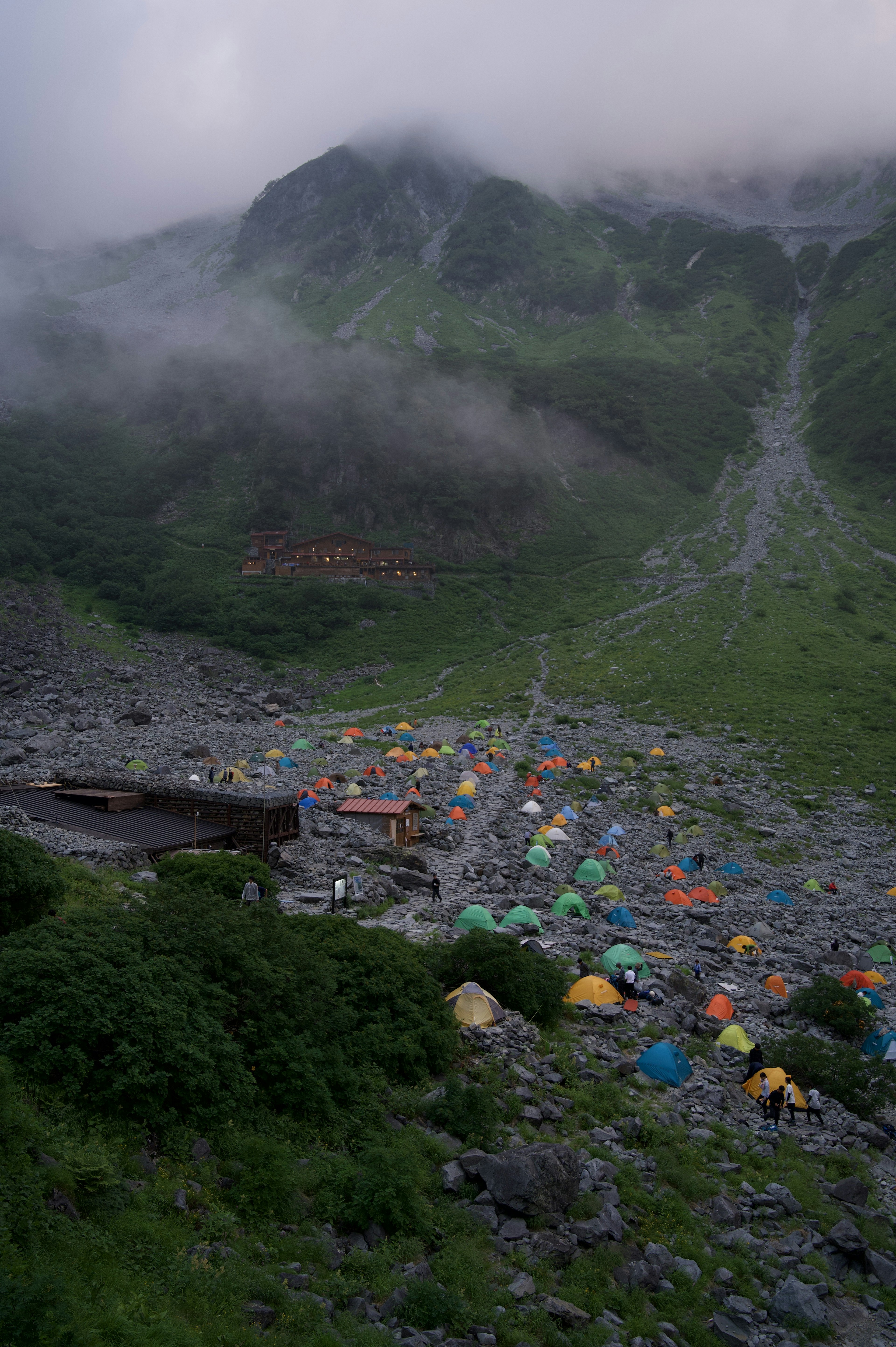 Colorful tents spread across a misty mountain valley with green hills