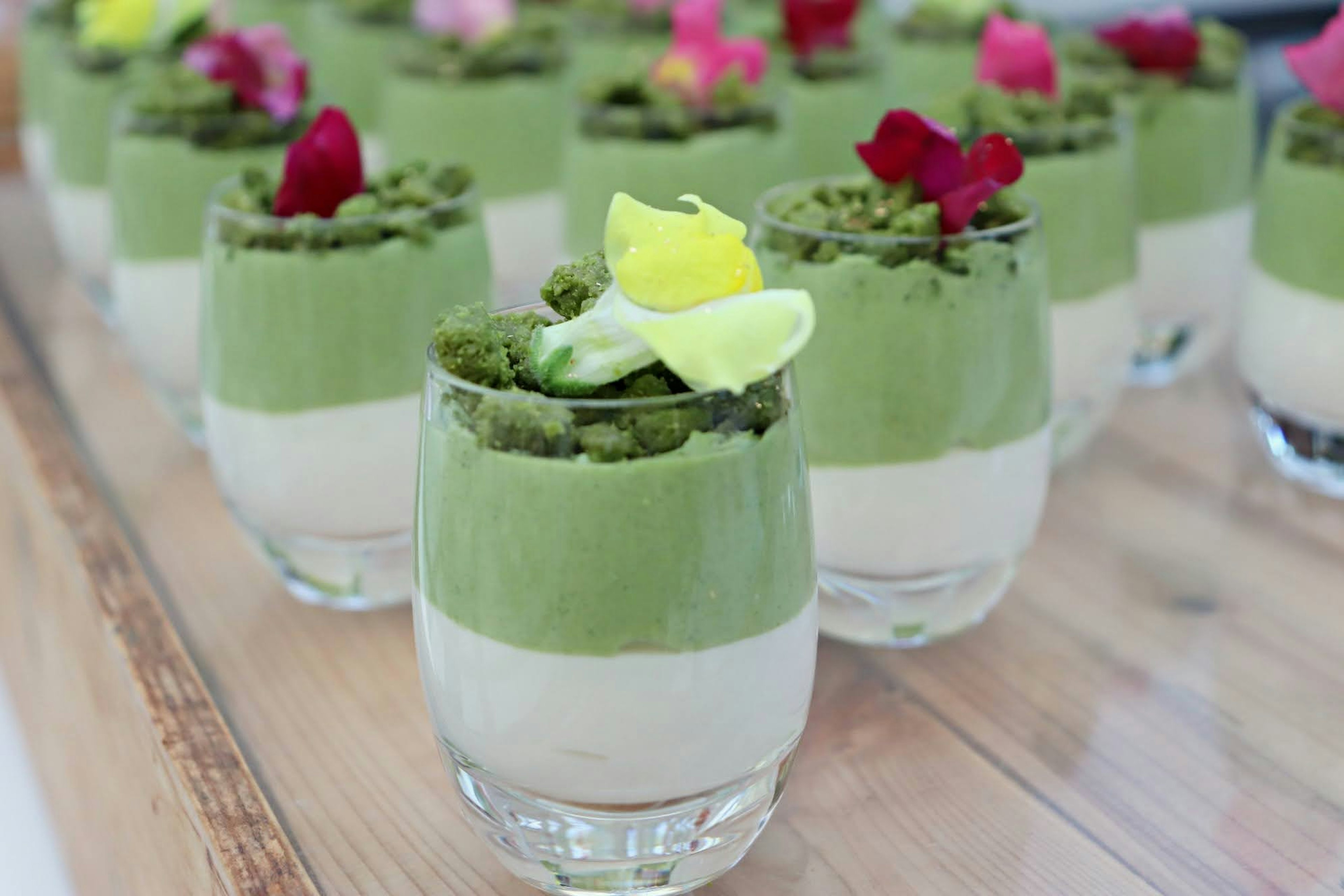 Bicchieri di dessert con strati di crema al matcha verde e crema bianca guarniti con fiori commestibili