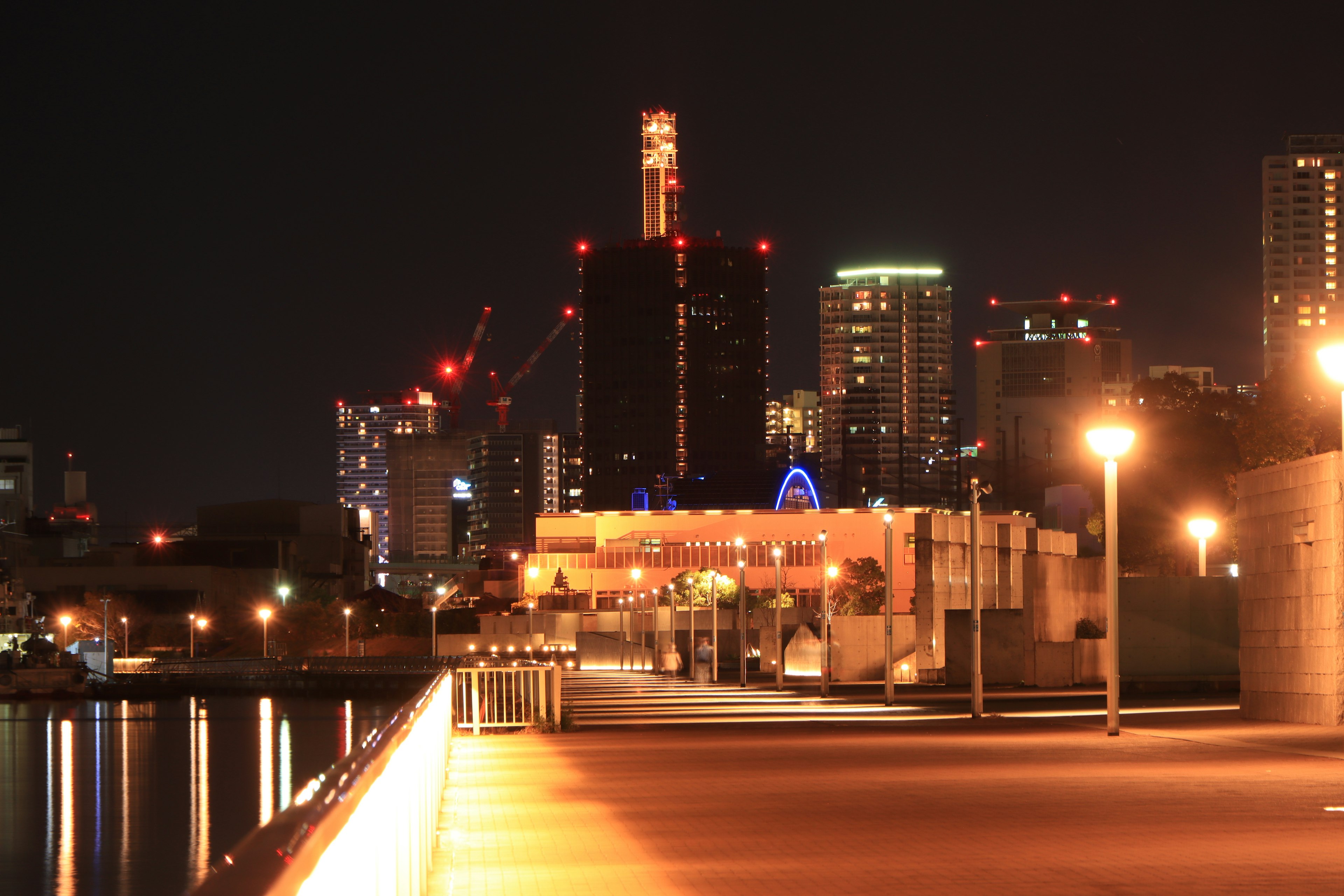 ทิวทัศน์เมืองยามค่ำคืนพร้อมไฟถนนสว่างบนทางเดินข้างแม่น้ำ