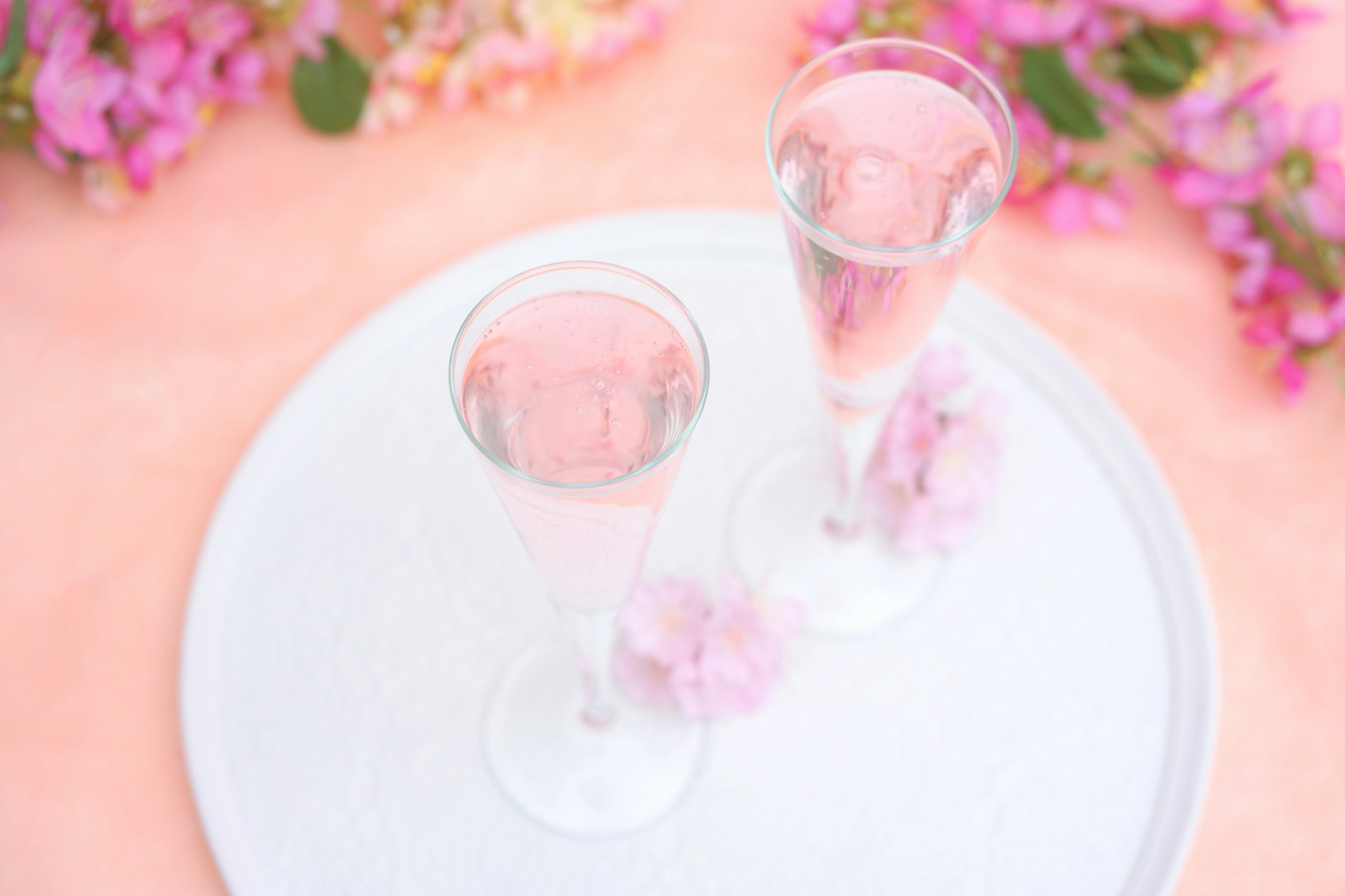 Zwei klare Gläser mit Wasser umgeben von rosa Blumen