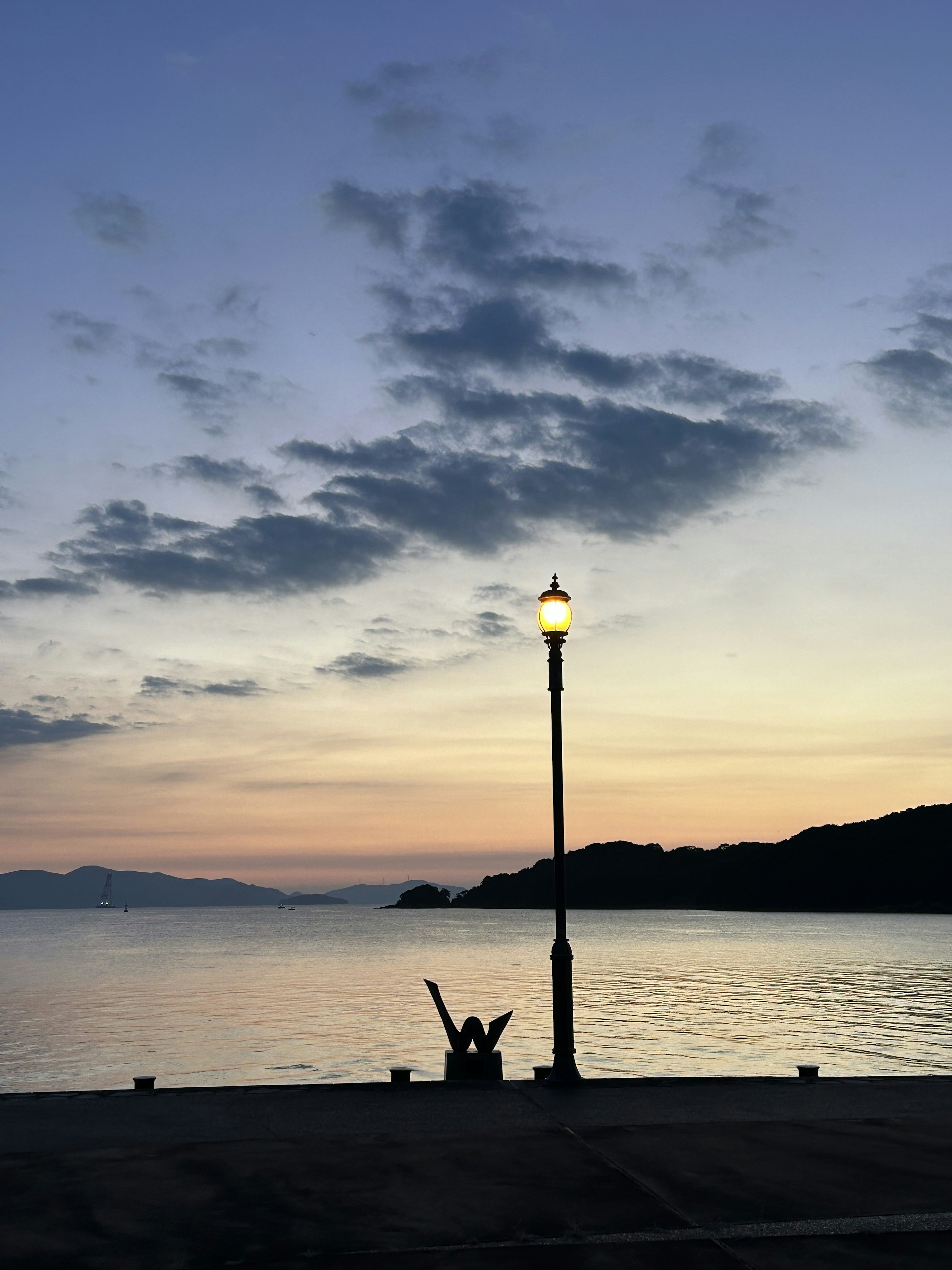 Eine Straßenlaterne am Wasser während des Sonnenuntergangs mit ruhigen Reflexionen